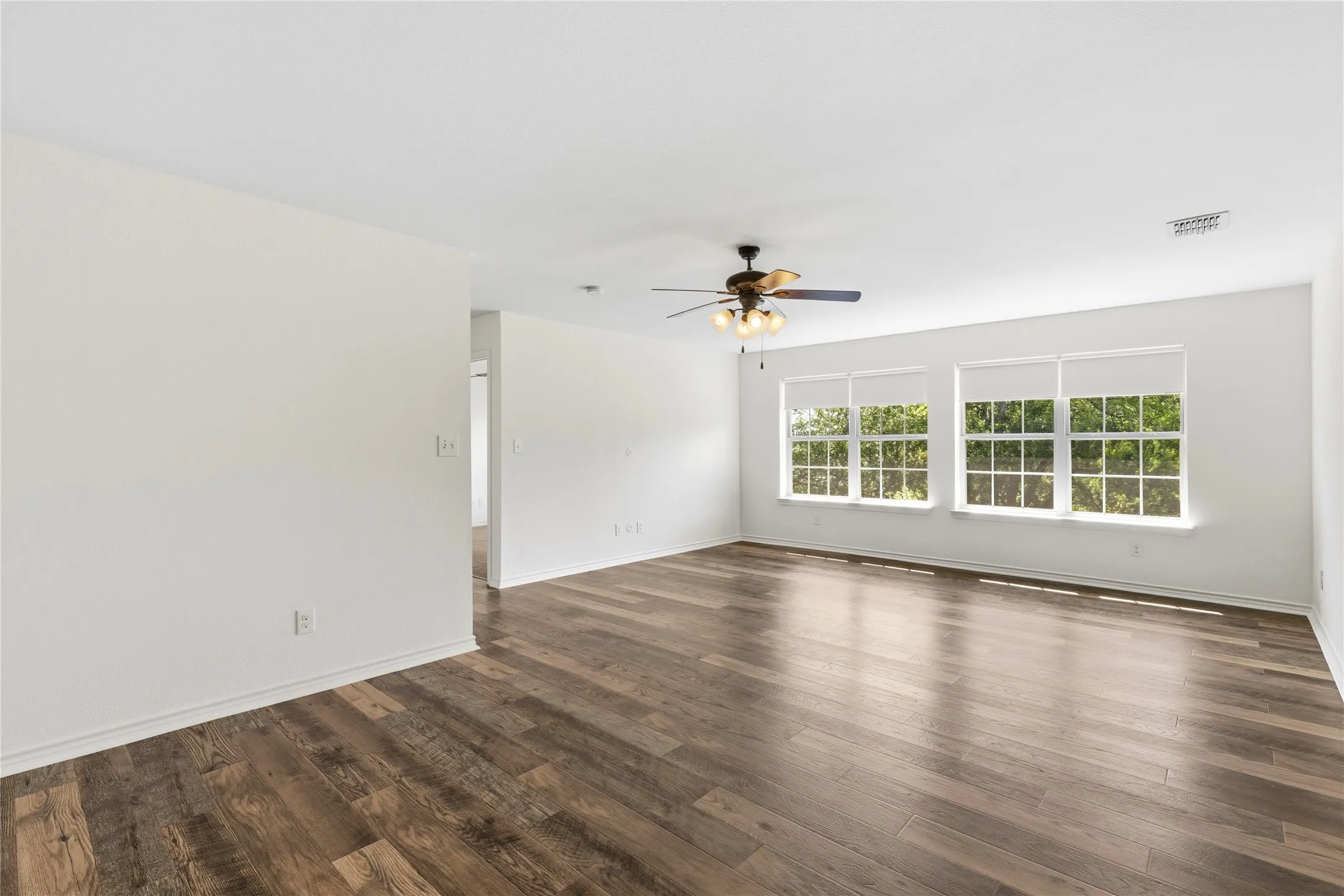 Spacious interior featuring wood-finish flooring, white walls, and multiple windows with roller shades