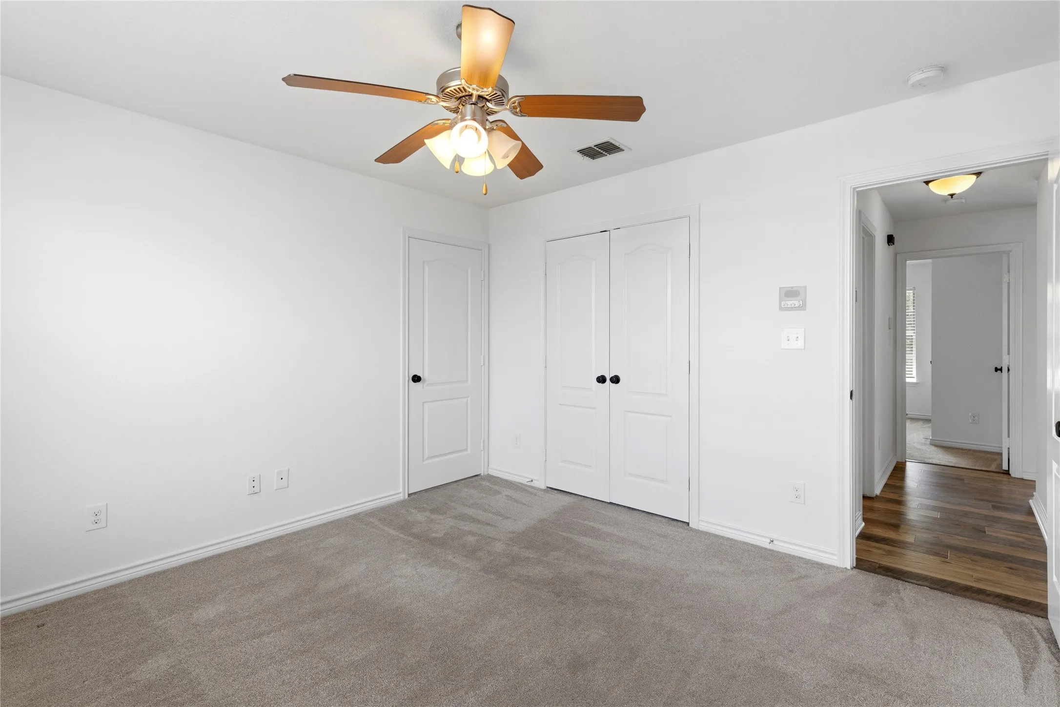 Neutral gray carpeted room featuring a ceiling fan with integrated lighting, a double-door closet, and a white paneled door