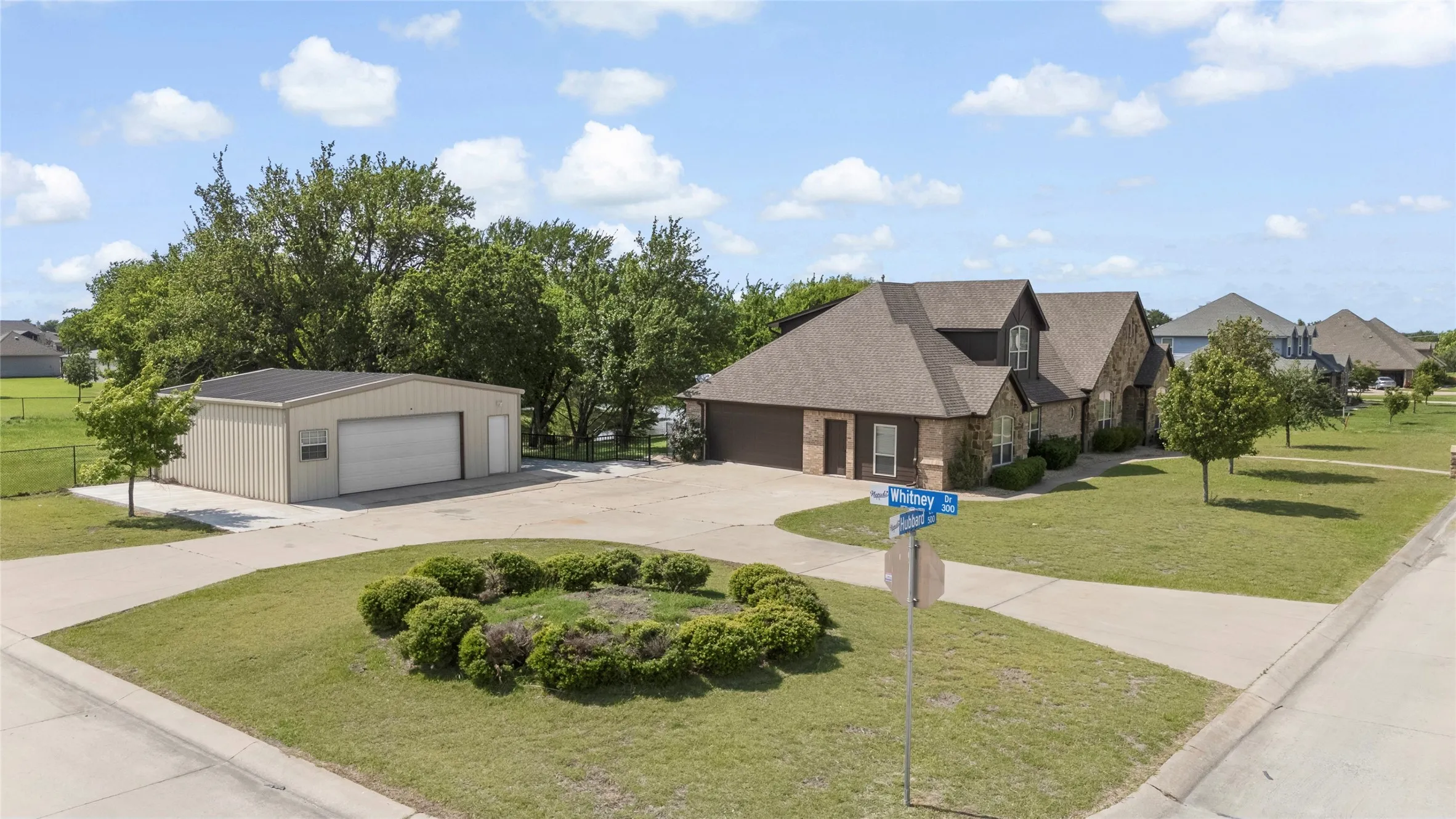 Spacious property featuring a brick and siding residence with a dark shingle roof, an attached two-car garage, and a separate large metal outbuilding with a roll-up door