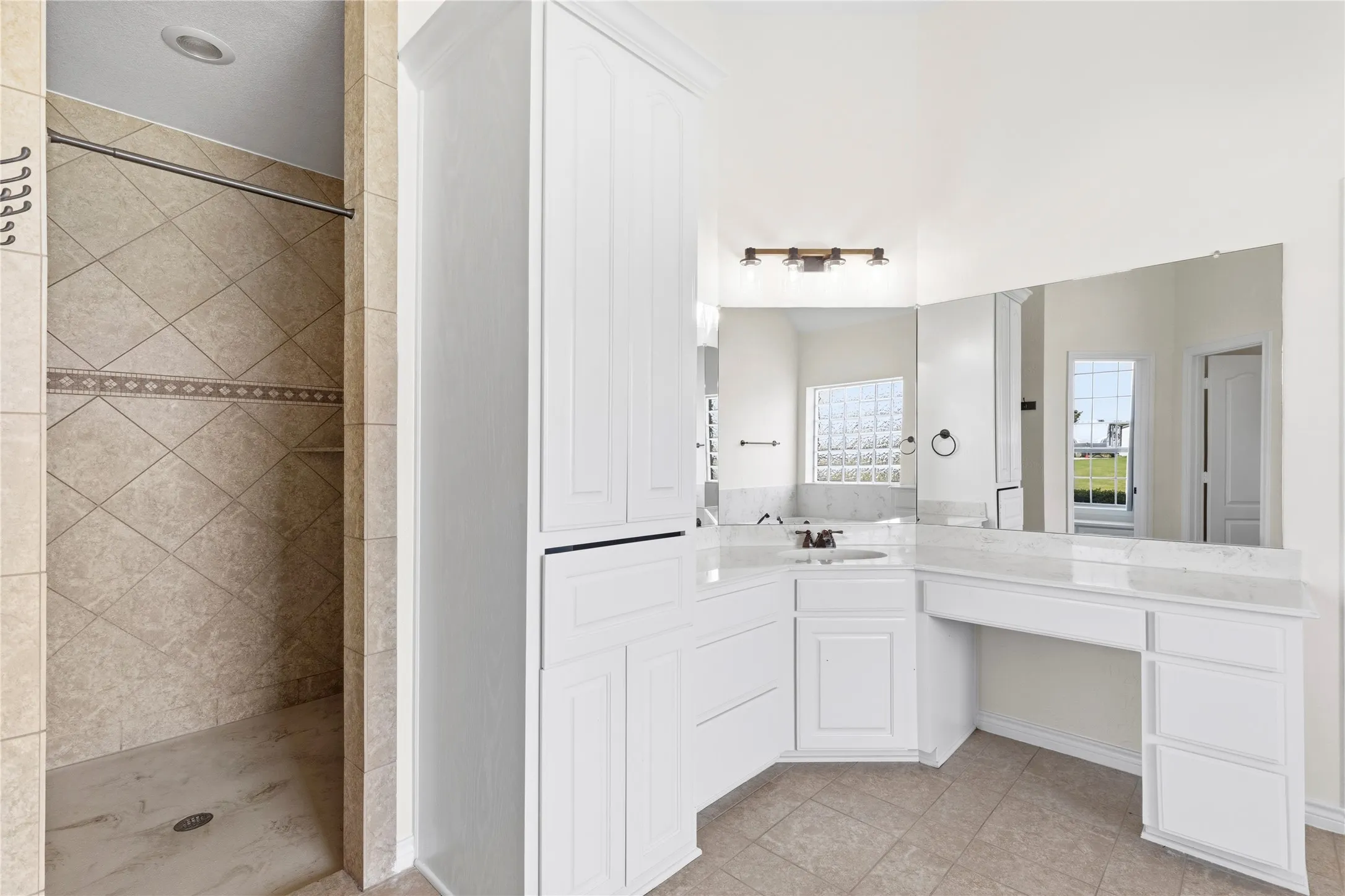 Spacious vanity area featuring white cabinetry with a built-in dressing table, expansive wall-mounted mirror, and a single basin with a contemporary faucet