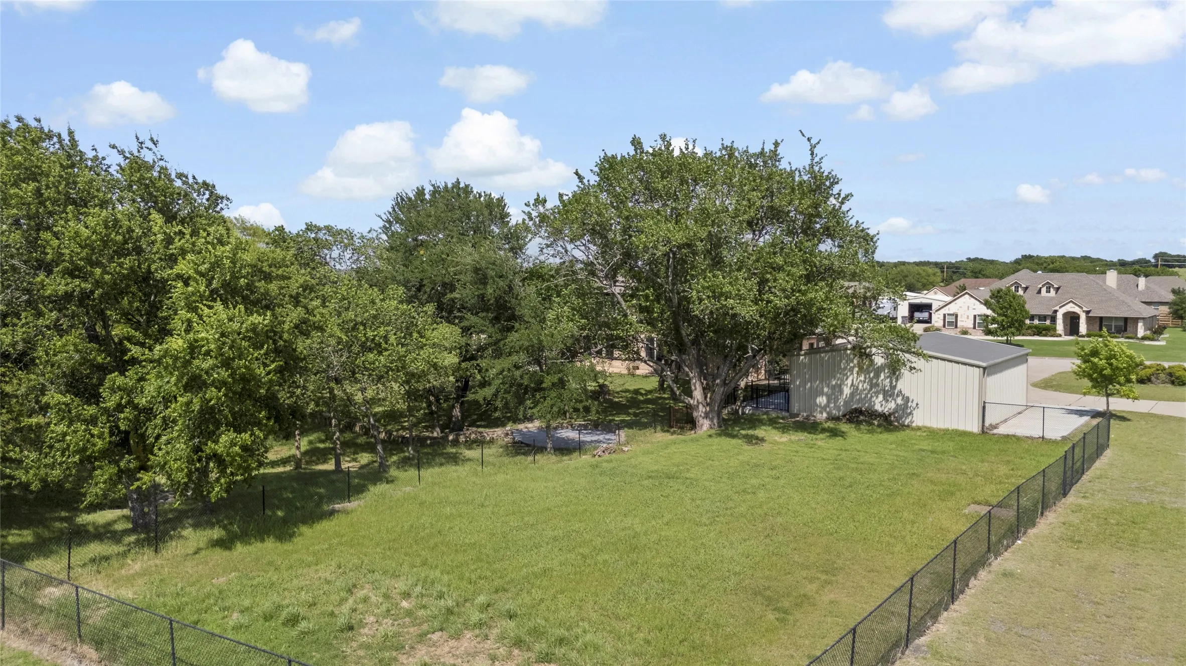 Expansive outdoor area featuring a metal utility shed, mature trees, and perimeter fencing