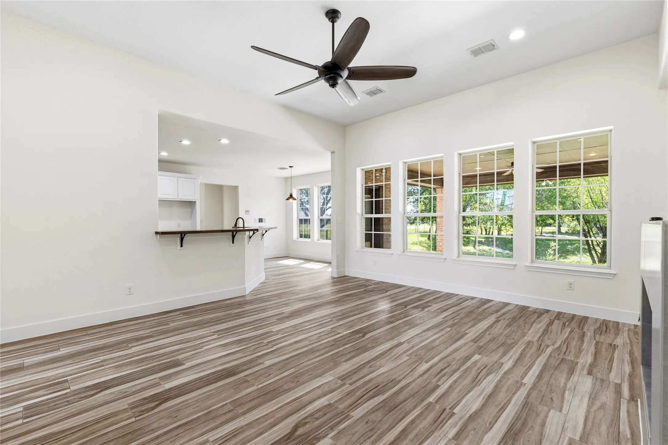 Spacious living area featuring wood-look tile flooring, a dark-toned ceiling fan, and recessed lighting