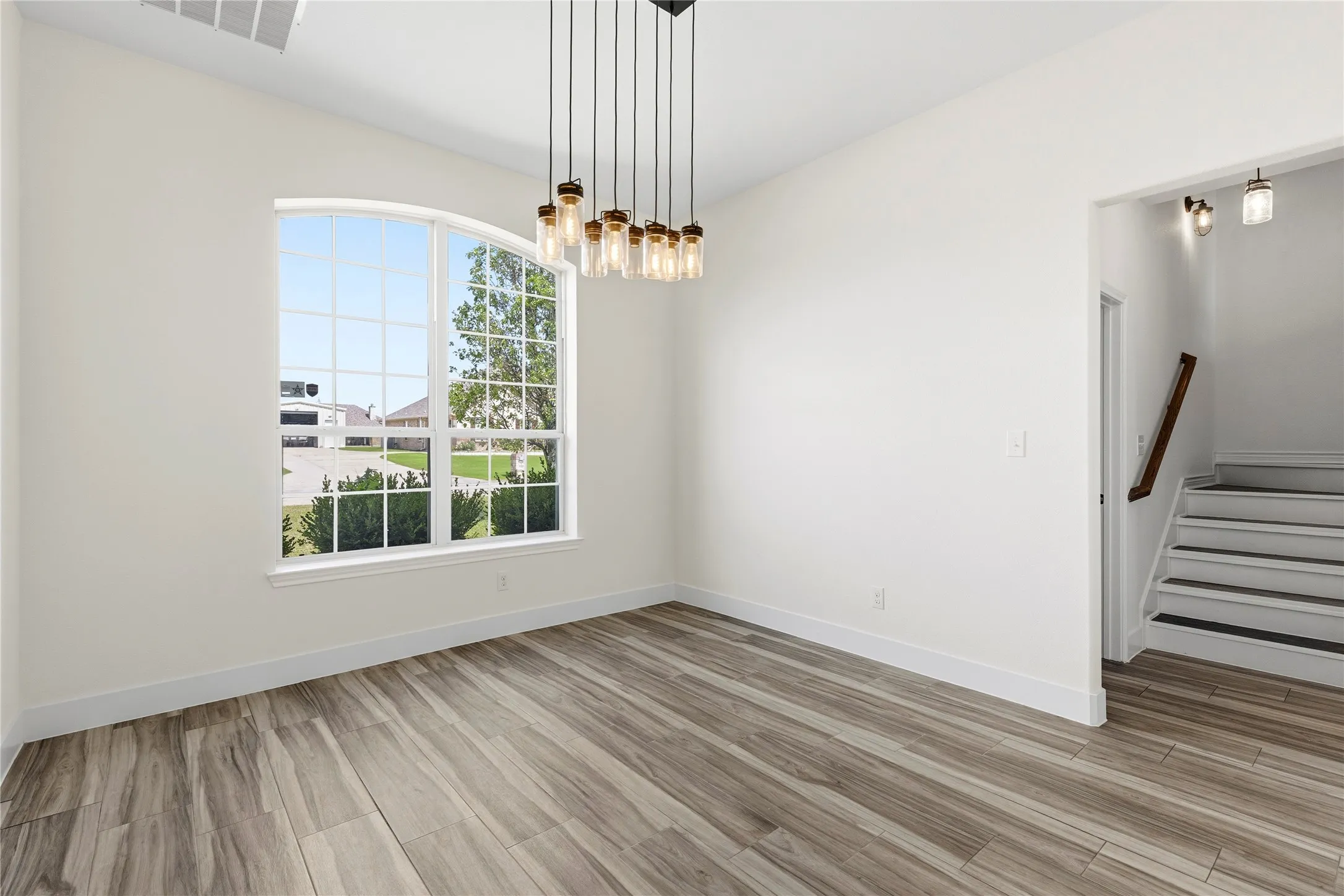 Room featuring an arched grid window, wood-finish flooring, and a contemporary multi-bulb chandelier