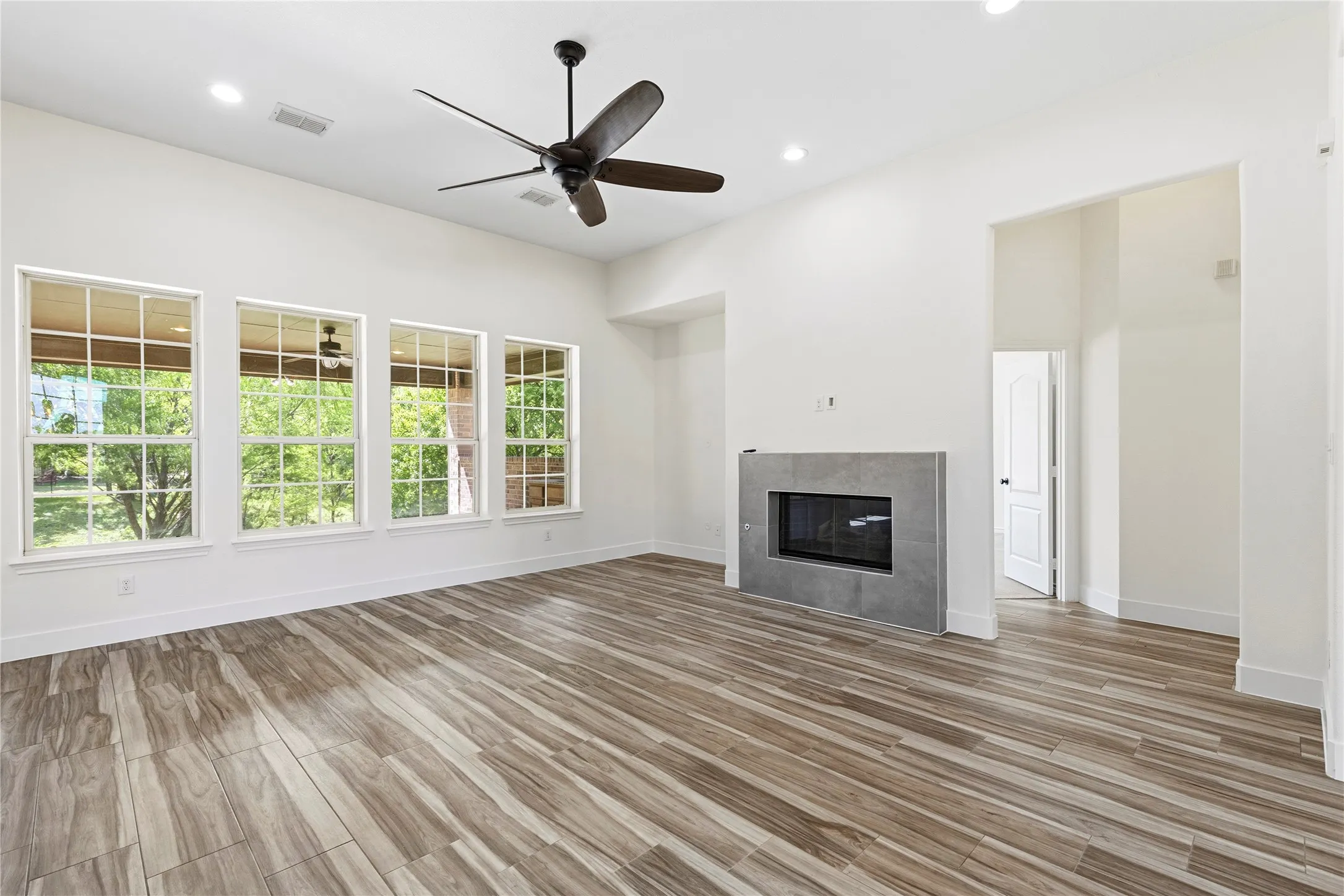 Spacious interior featuring wood-finish flooring, a modern fireplace with a tiled surround, recessed lighting, and a ceiling fan
