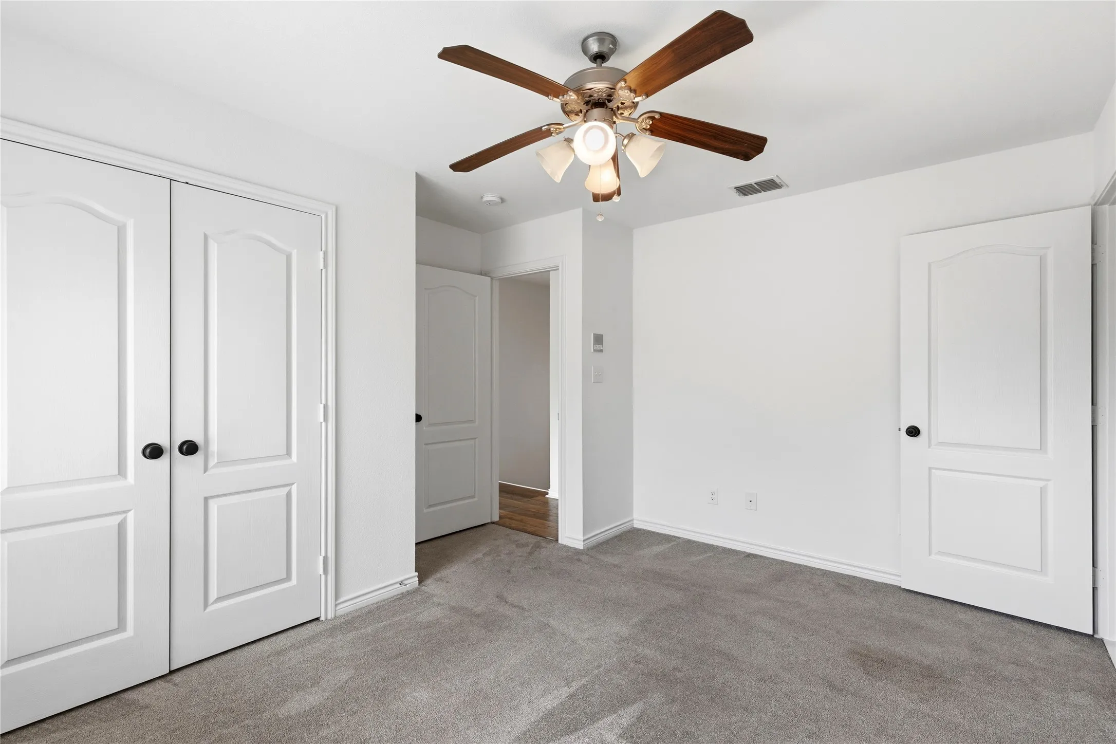 Carpeted room featuring a ceiling fan with light kit, bi-fold closet doors, white paneled doors, and white baseboards