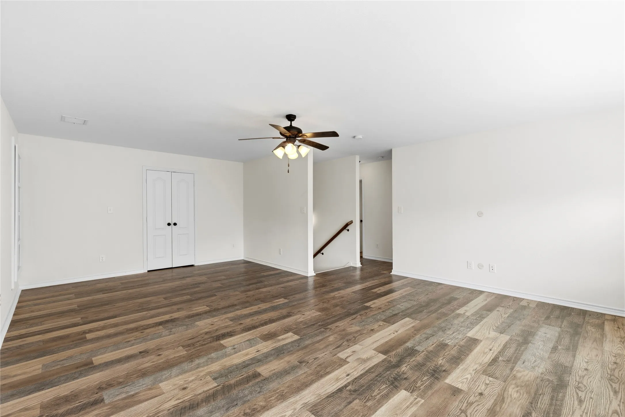 Spacious room featuring wood-finish flooring, light-toned walls, a ceiling fan with integrated lighting, and white bi-fold closet doors with dark hardware