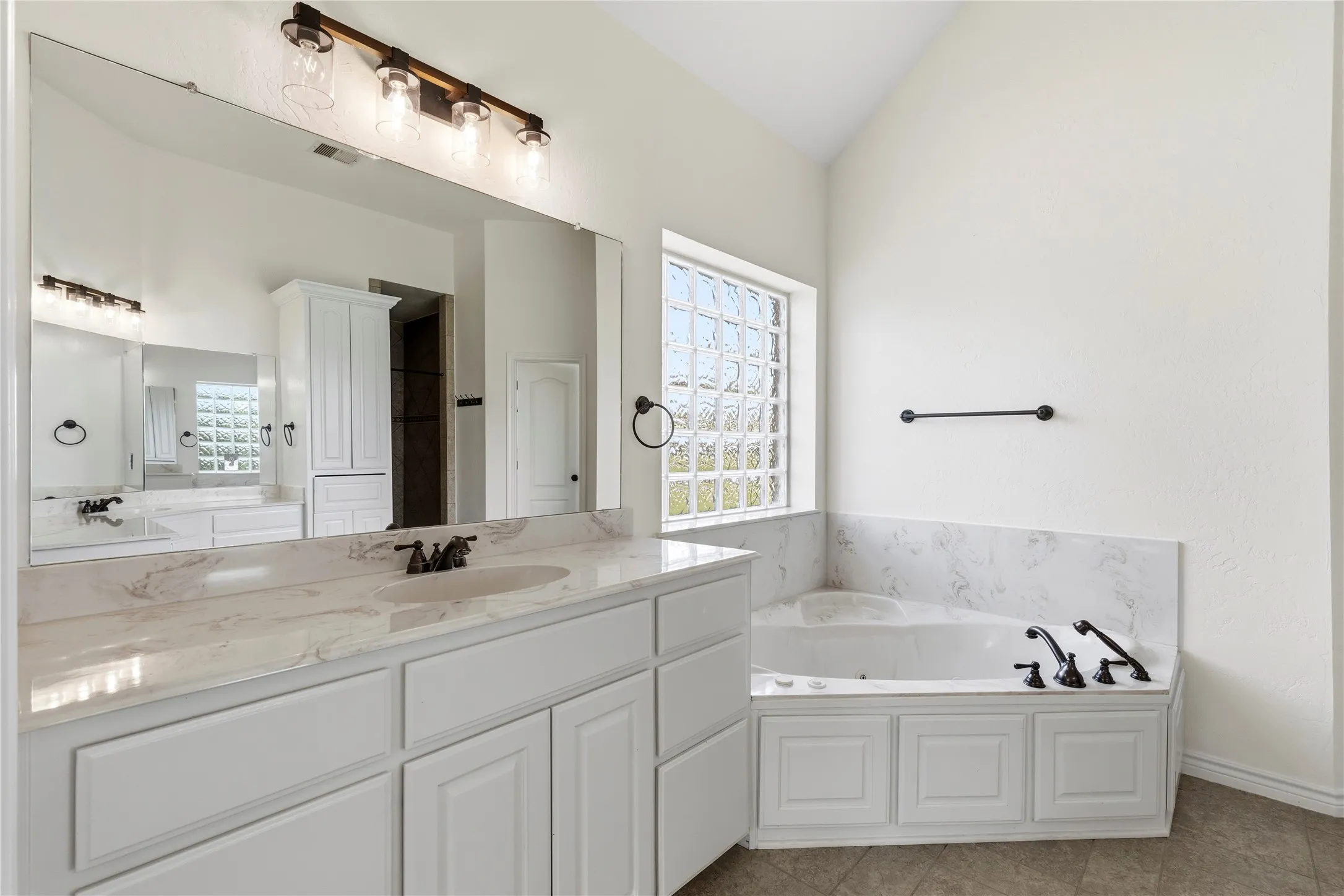 Spacious bathroom featuring an expansive vanity with double sinks, white cabinetry, and a light-toned countertop
