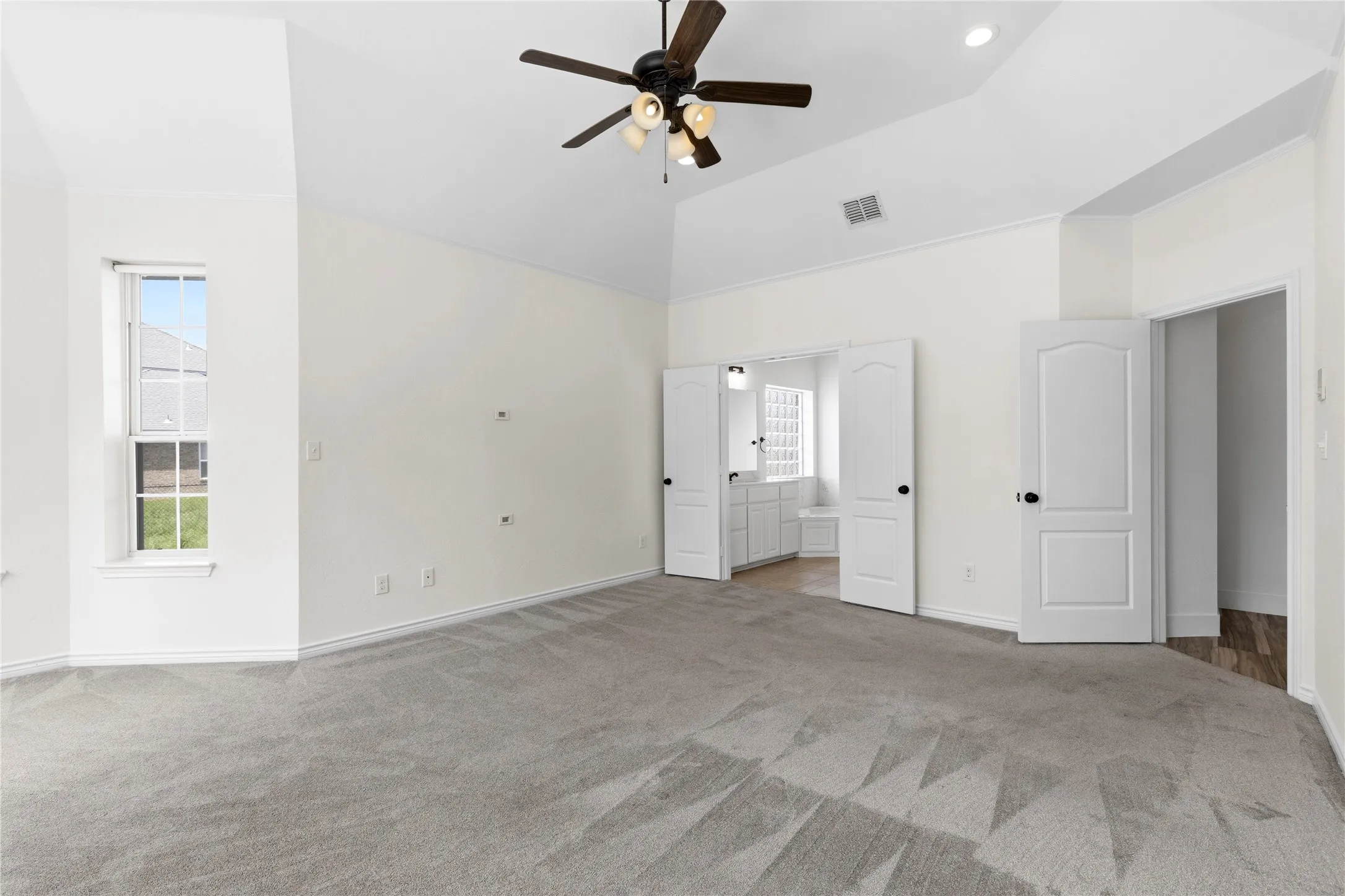 Spacious room featuring vaulted ceilings, a ceiling fan with light fixture, light gray carpeting, and a window with a white frame