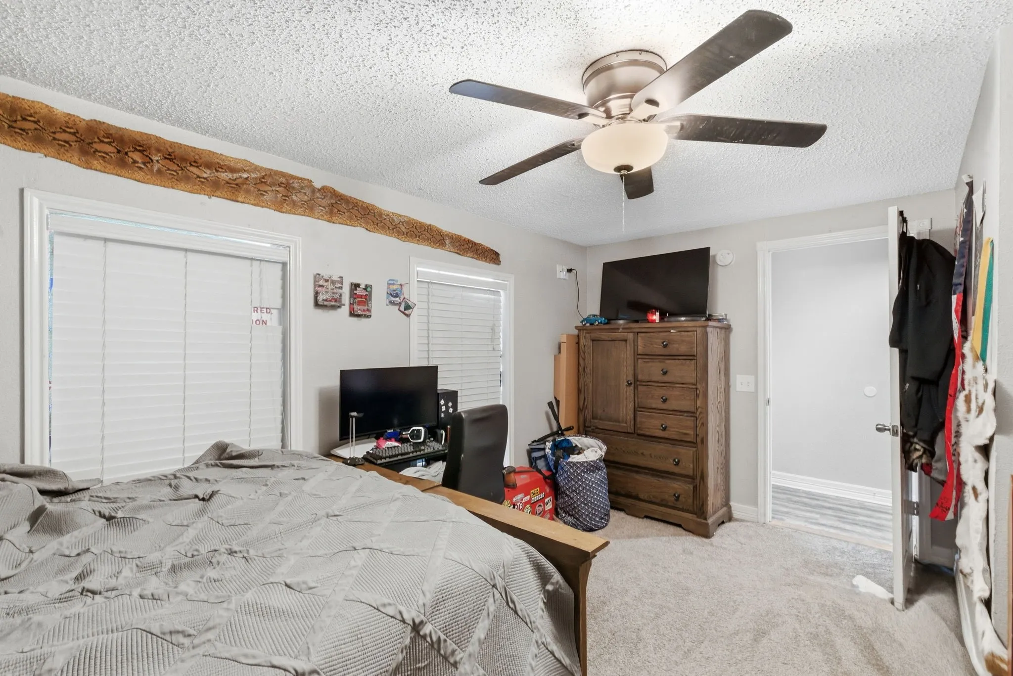 Bright room featuring two windows with horizontal blinds, a ceiling fan with integrated lighting, and light-colored carpet flooring