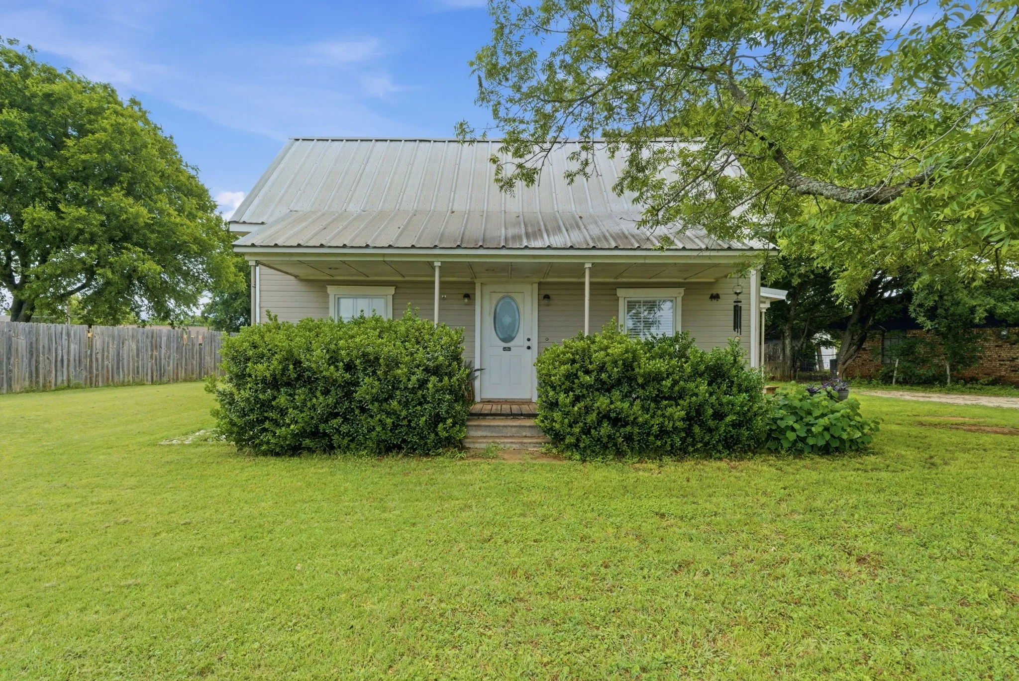 Single-story residence featuring a metal roof, a covered front porch, and mature landscaping