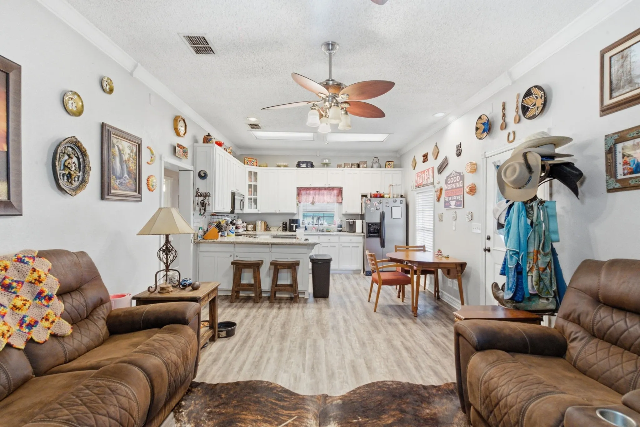 Open-concept living area featuring wood-finish flooring, a ceiling fan with integrated lighting, and crown molding