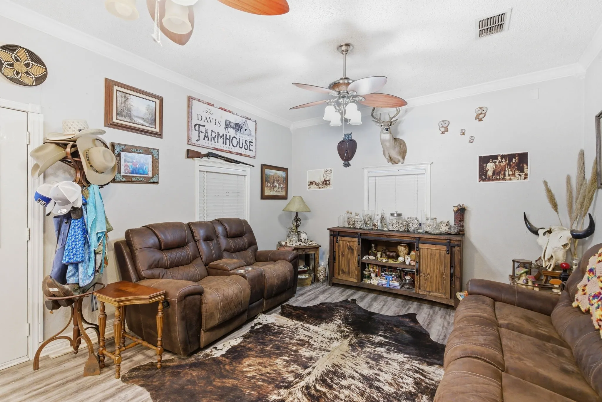 Living area featuring wood-finish flooring, a ceiling fan with light fixture, and crown molding