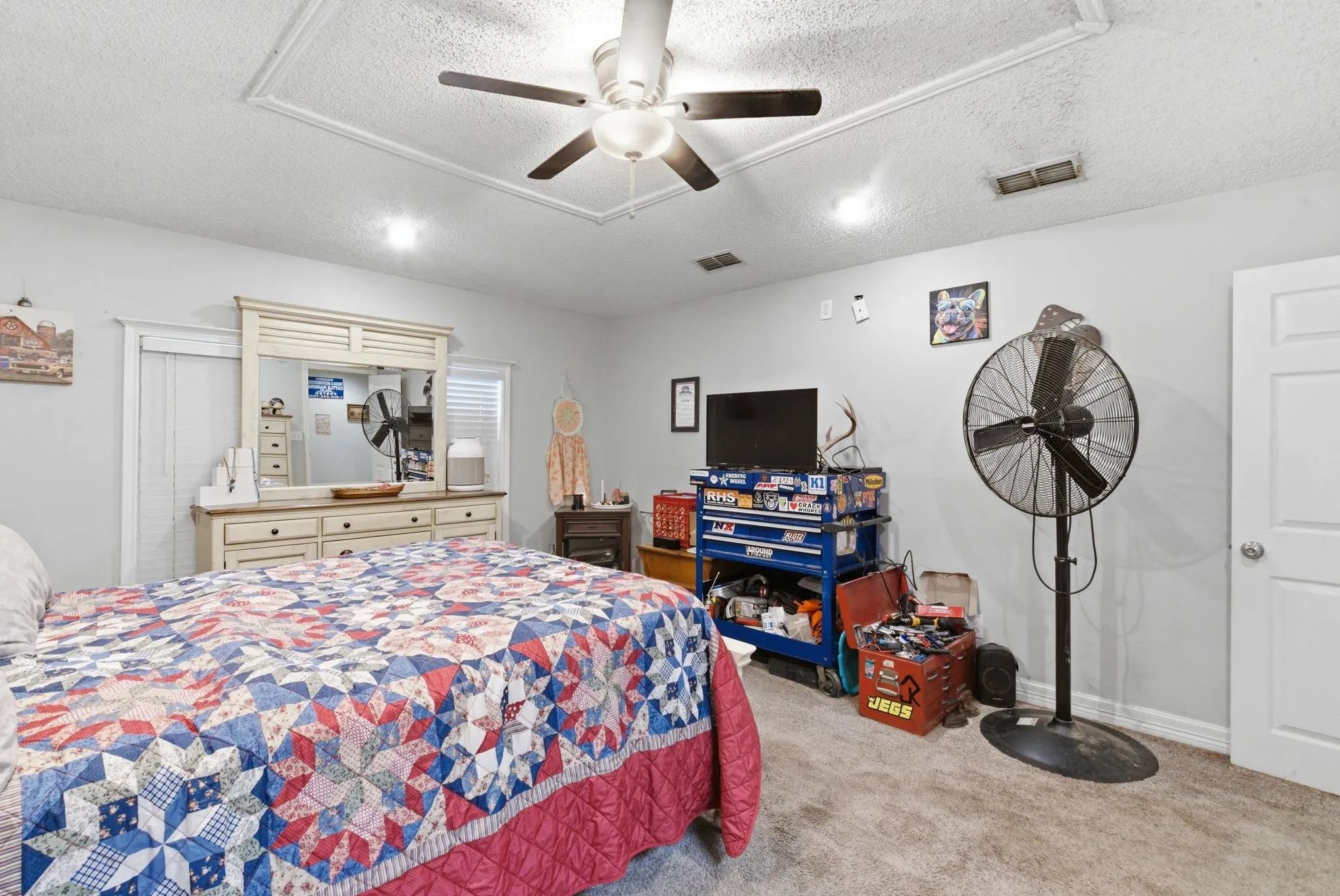 Carpeted bedroom featuring a tray ceiling, ceiling fan with light fixture, and light gray wall paint