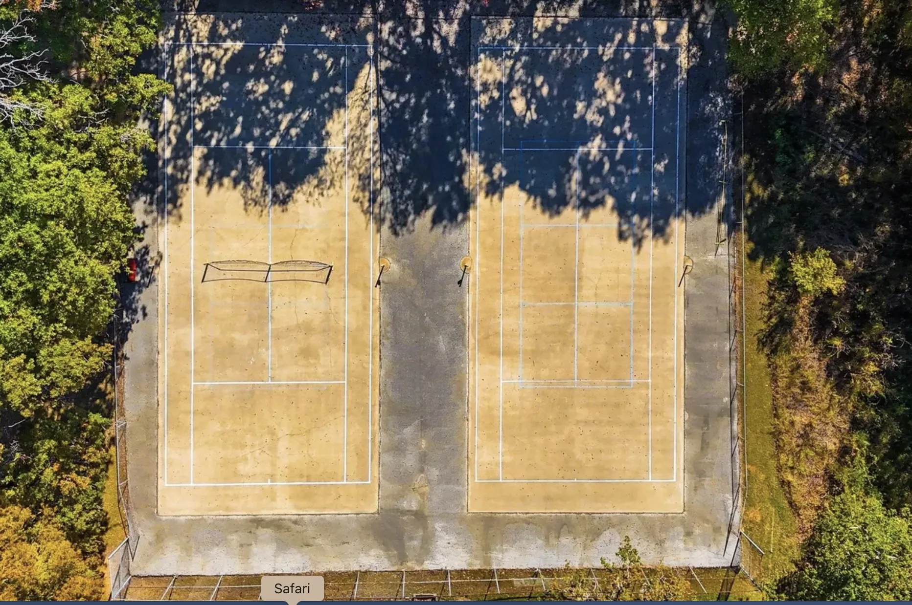 Two hard-surface tennis courts featuring perimeter fencing and surrounded by mature trees