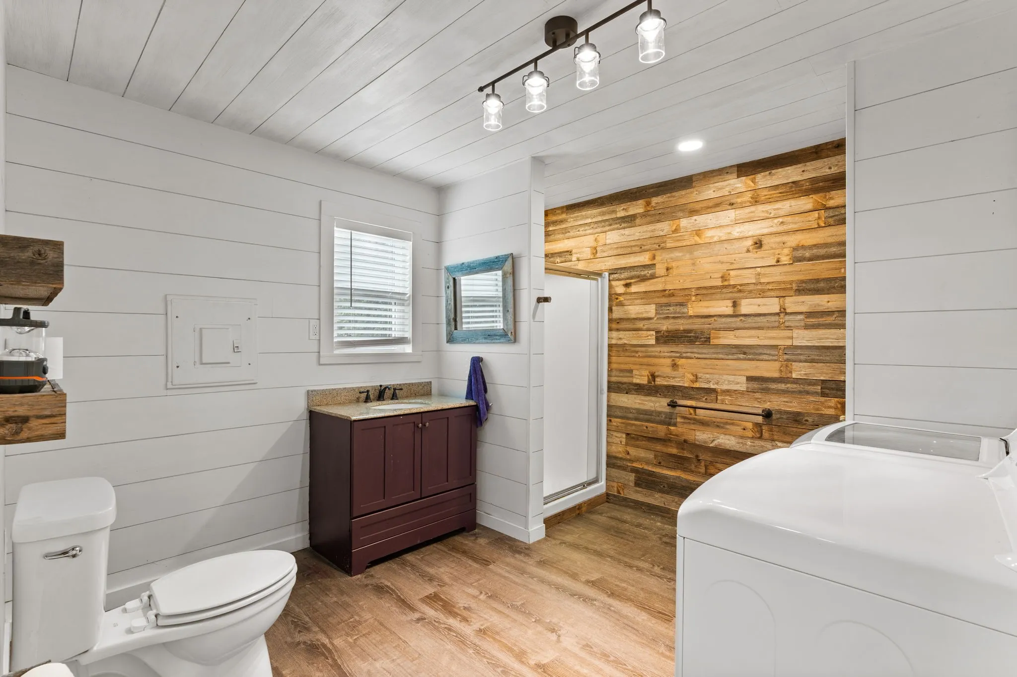 Bathroom featuring shiplap walls, wood-finish flooring, a rustic wood accent wall, a track lighting fixture, and a built-in vanity with a countertop