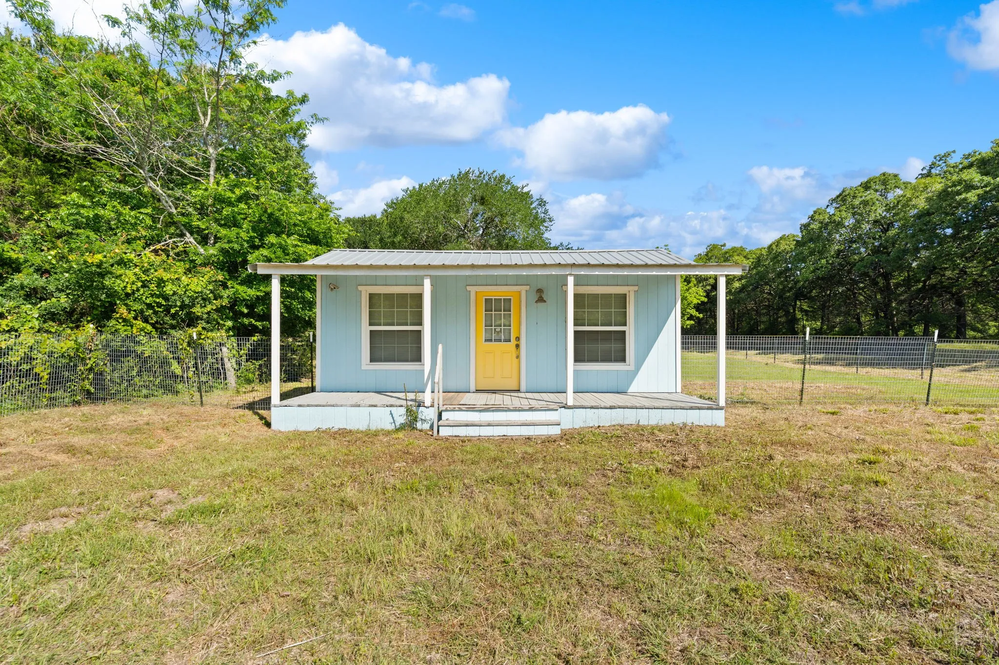 Light blue exterior with a bright yellow second structureentrance door and a covered front porch