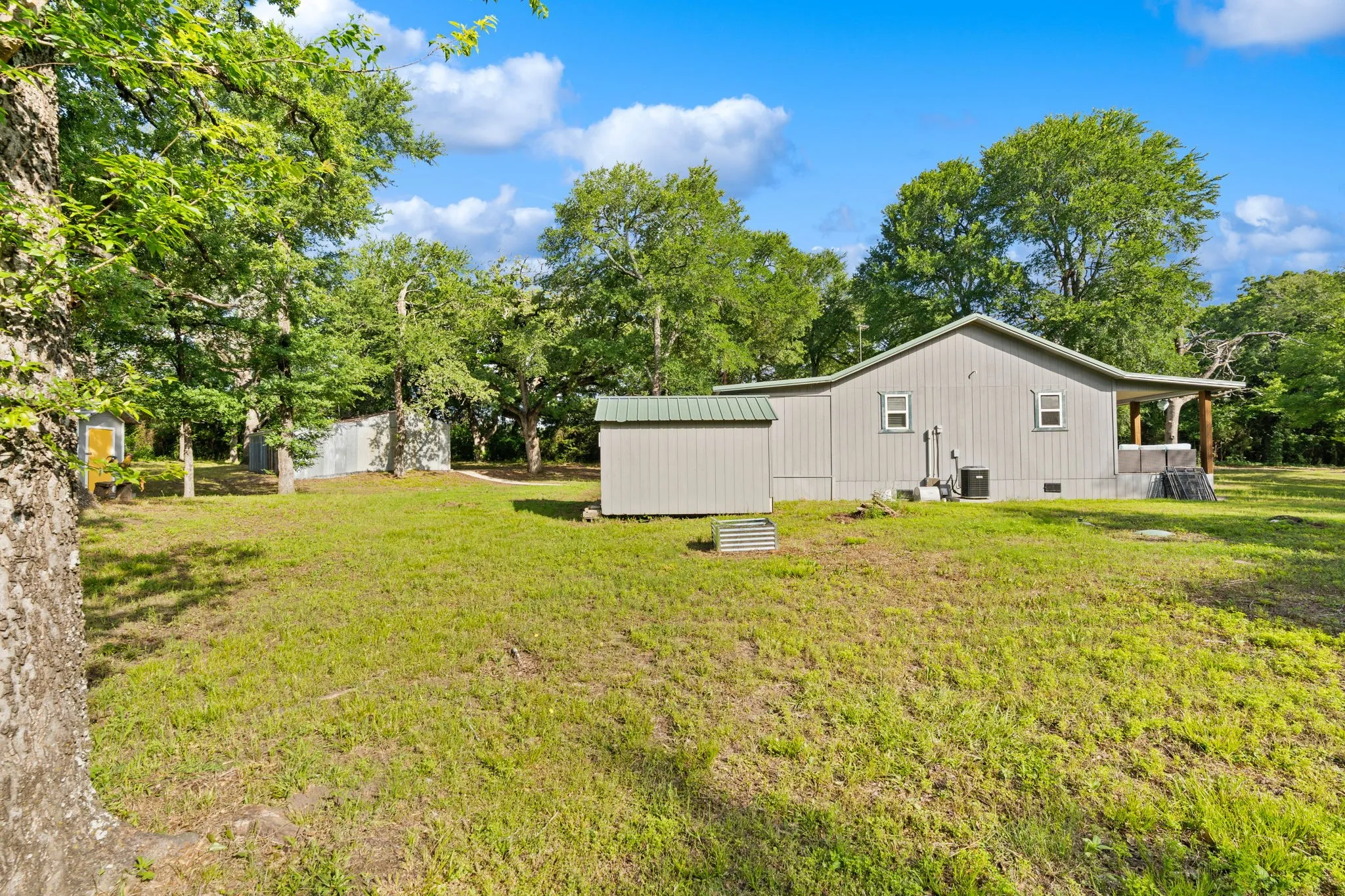 Expansive rear property featuring a single-story structure with siding, an attached covered porch, and multiple outbuildings