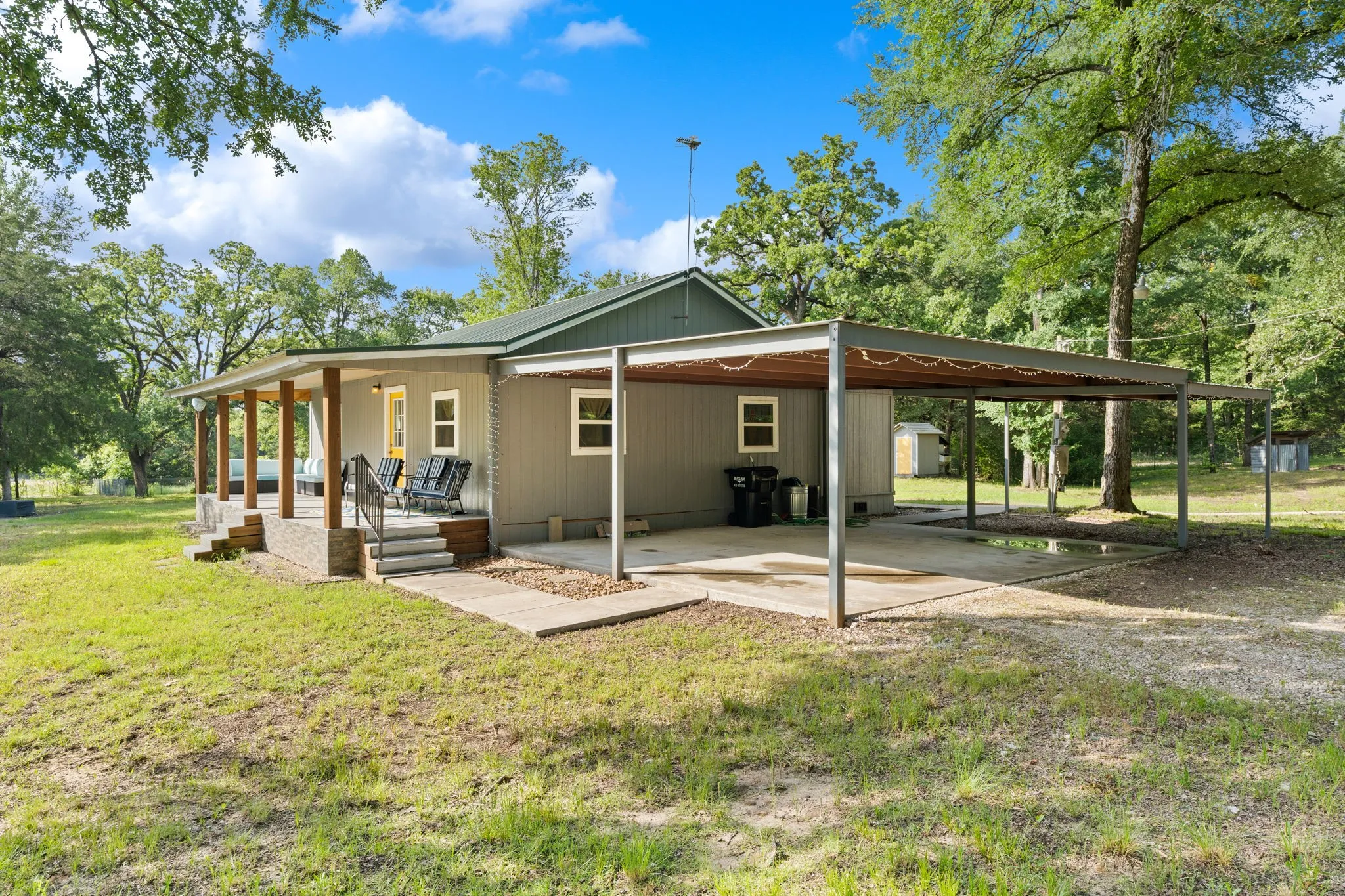 Exterior featuring a covered front porch with wood columns, a covered carport, and a light gray siding facade