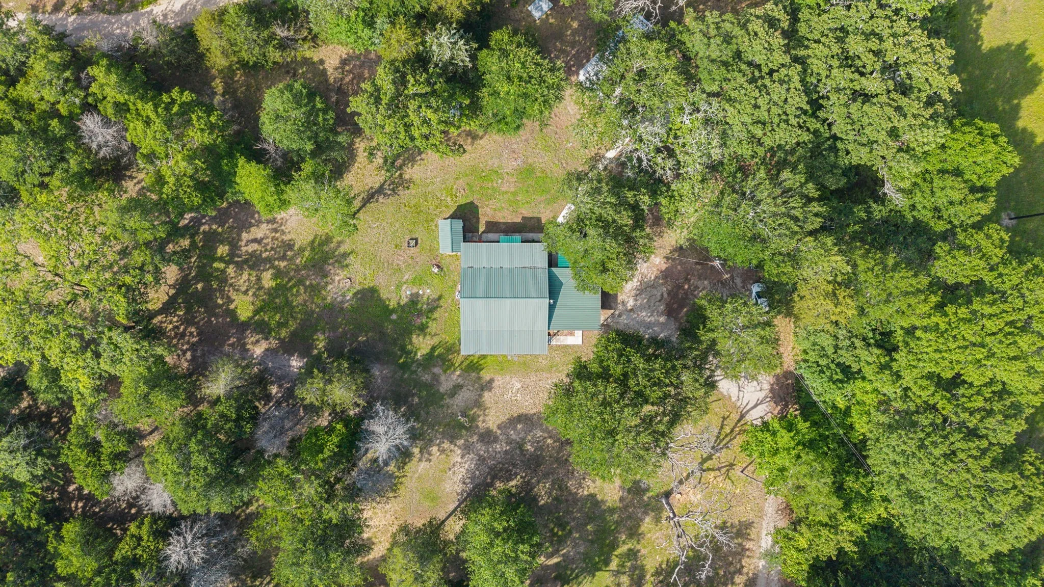 Aerial property image featuring a green metal roof structure surrounded by abundant mature trees and natural landscaping