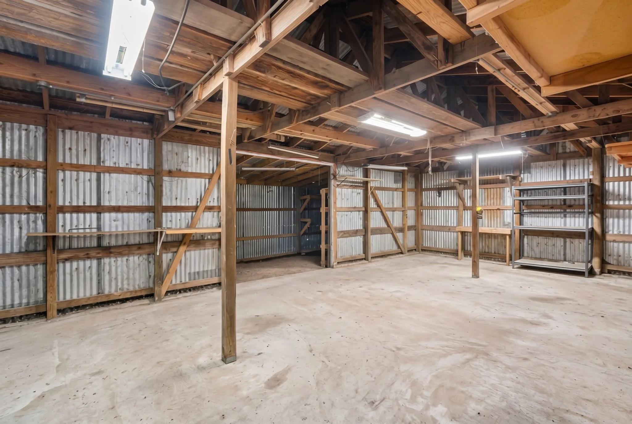 Interior space featuring exposed wood beam ceiling, corrugated metal wall panels, concrete flooring, and built-in shelving units