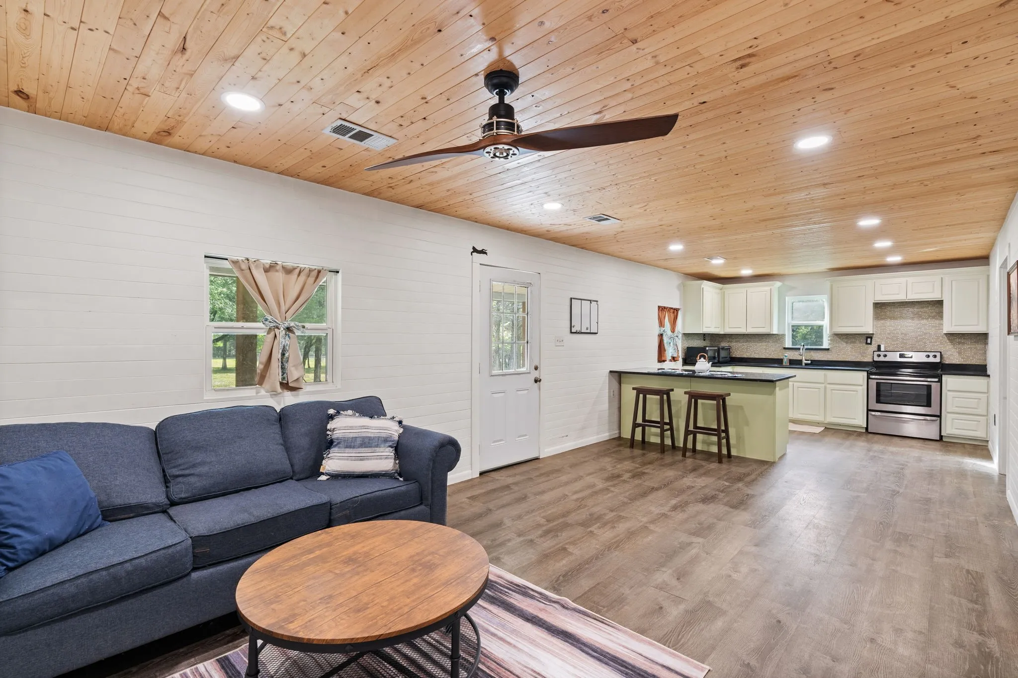 Open-concept living space featuring wood-finish flooring, a planked wood ceiling with recessed lighting, and a ceiling fan
