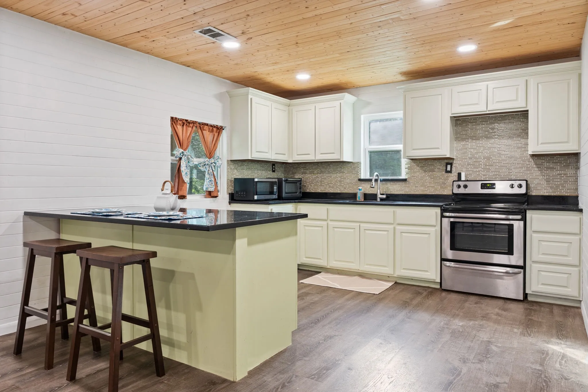 Kitchen featuring wood-finish flooring, light-toned cabinetry, stainless steel range, dark countertops, and a tiled backsplash