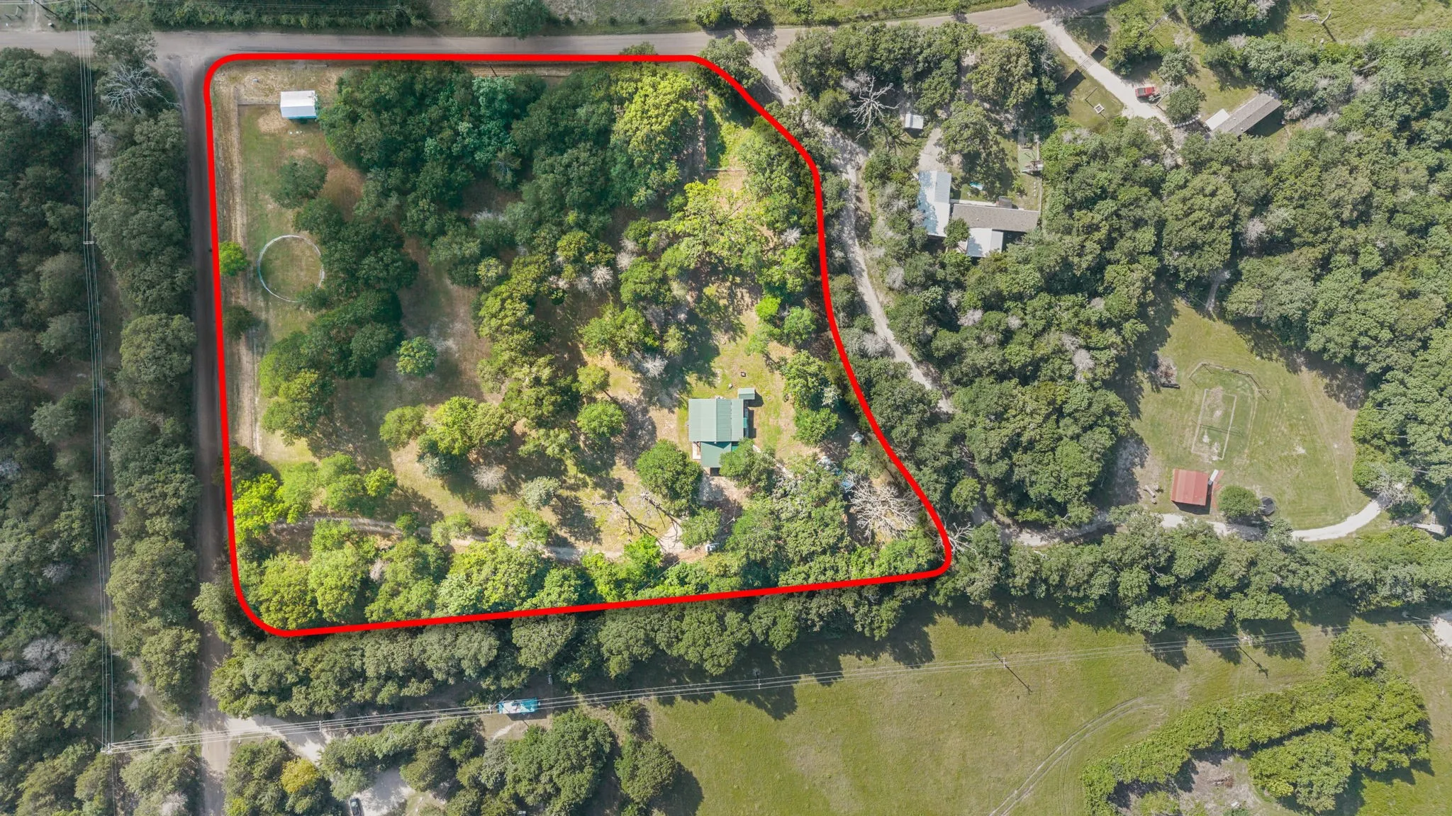 Expansive parcel featuring mature trees, a single-story residence with a green roof, outbuildings, and cleared areas