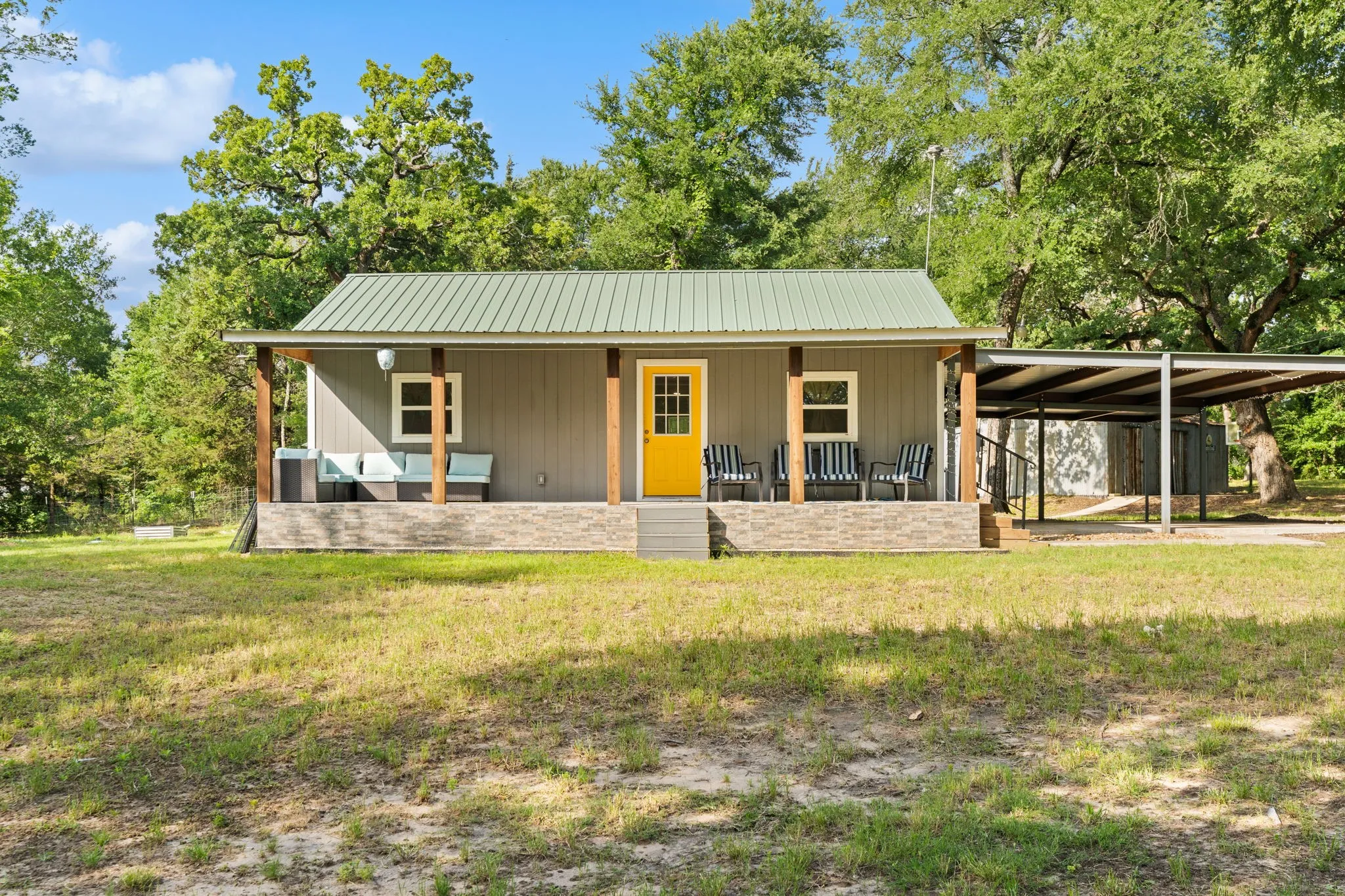Charming single-story residence featuring a covered front porch with wood columns, a vibrant yellow entry door, and a light gray siding exterior