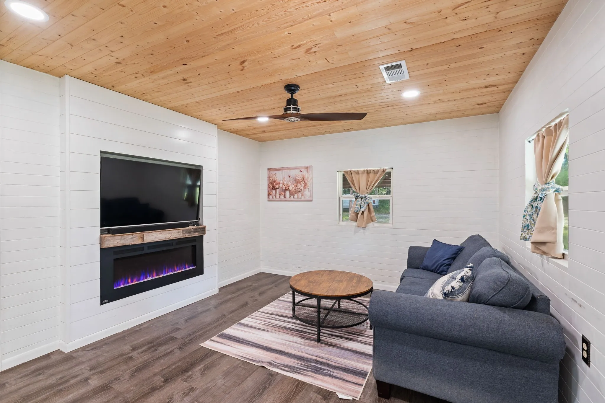 Feature wall with an integrated electric fireplace and mantle, shiplap wall treatment, wood-finish flooring, wood plank ceiling, and recessed lighting