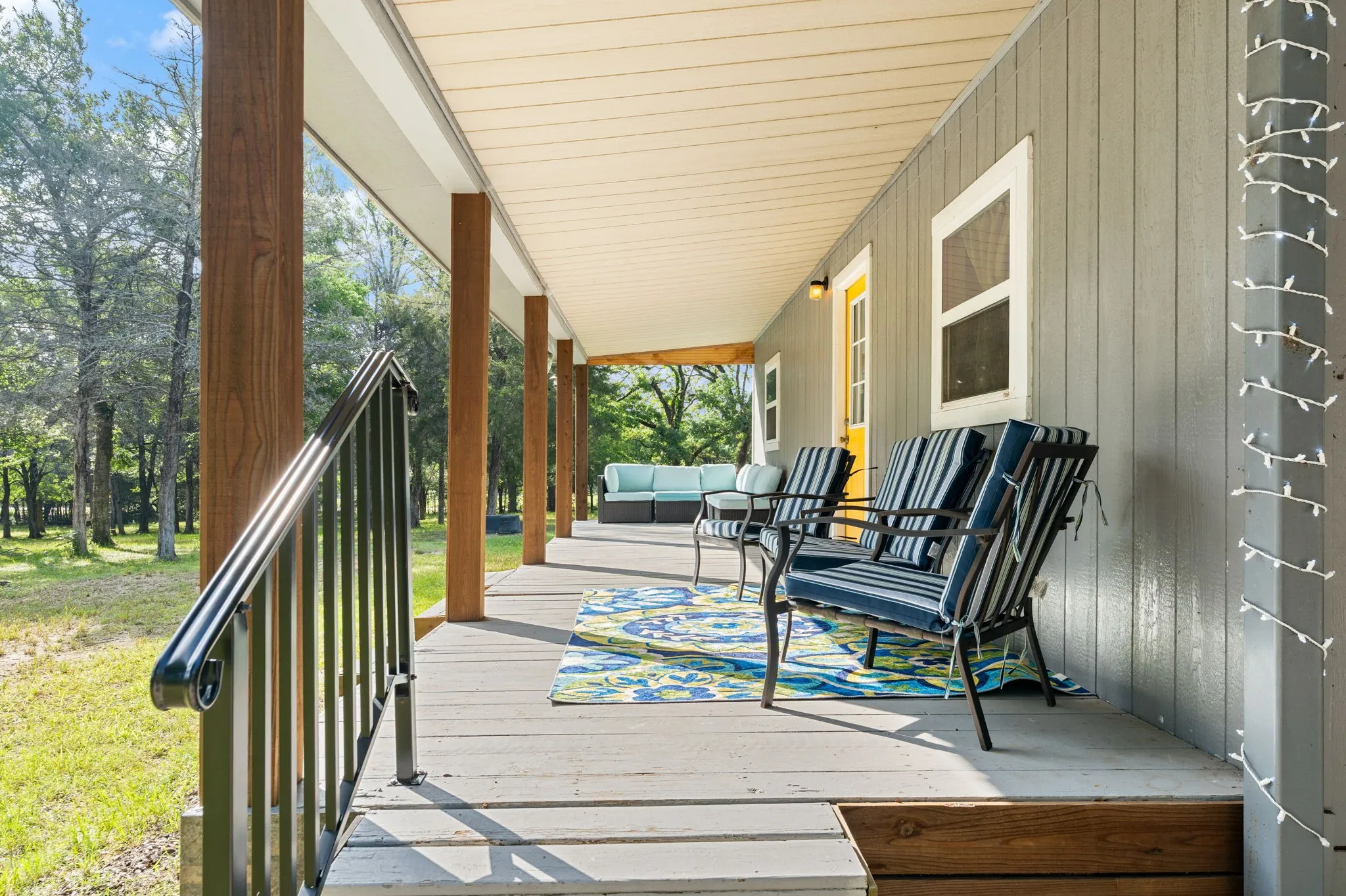 Expansive covered porch featuring wood-finish support columns, a black metal railing, and light gray vertical siding