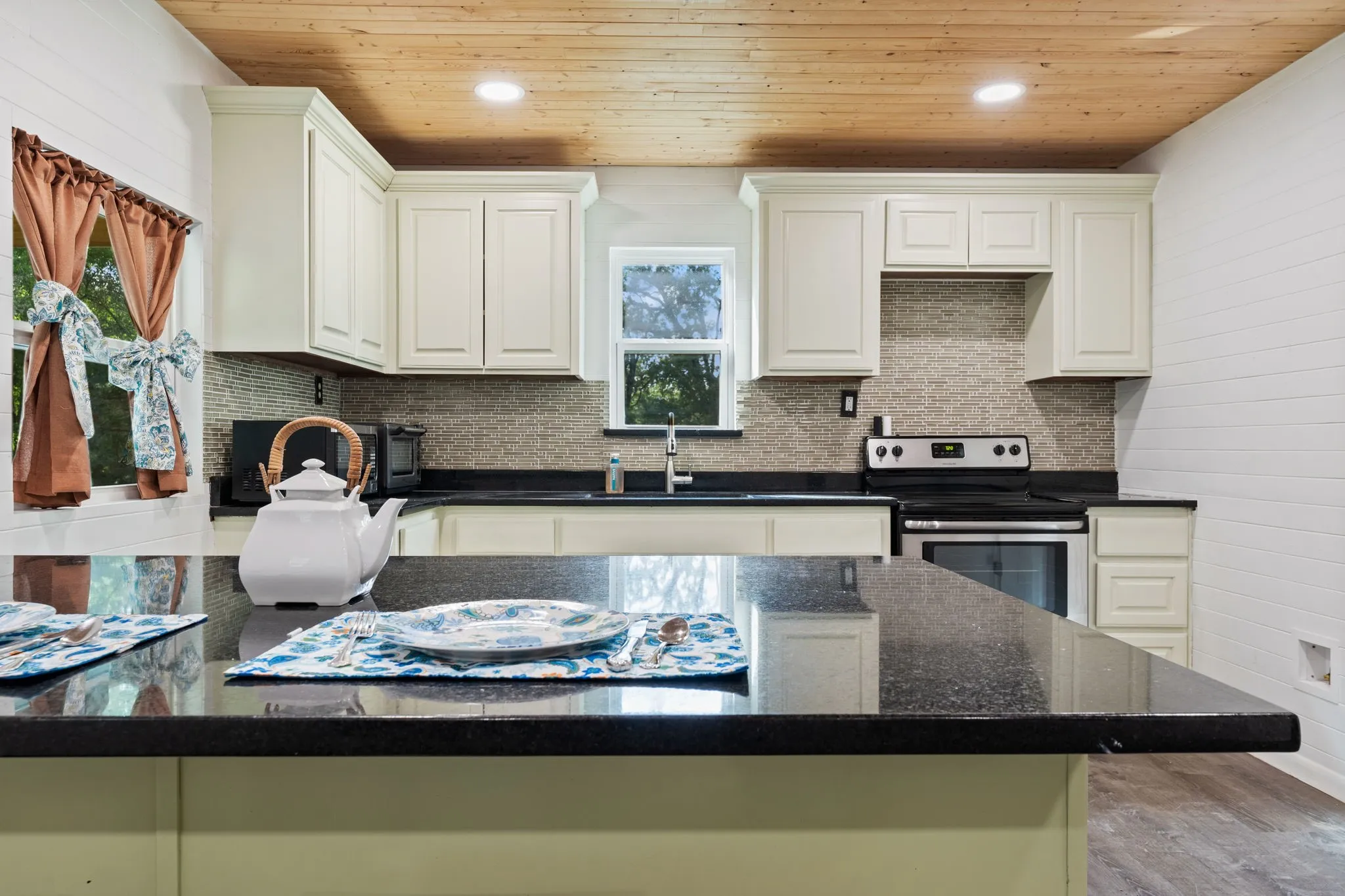 Kitchen featuring black countertops, light-toned cabinetry, a mosaic tile backsplash, and a wood-plank ceiling