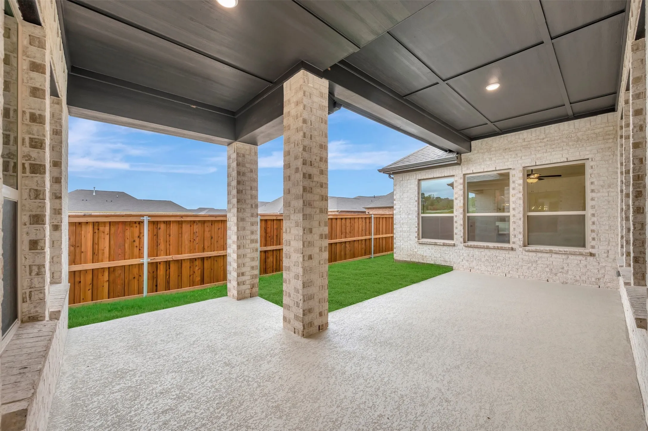 Covered patio with a textured concrete surface, brick columns, and a paneled ceiling with recessed lighting