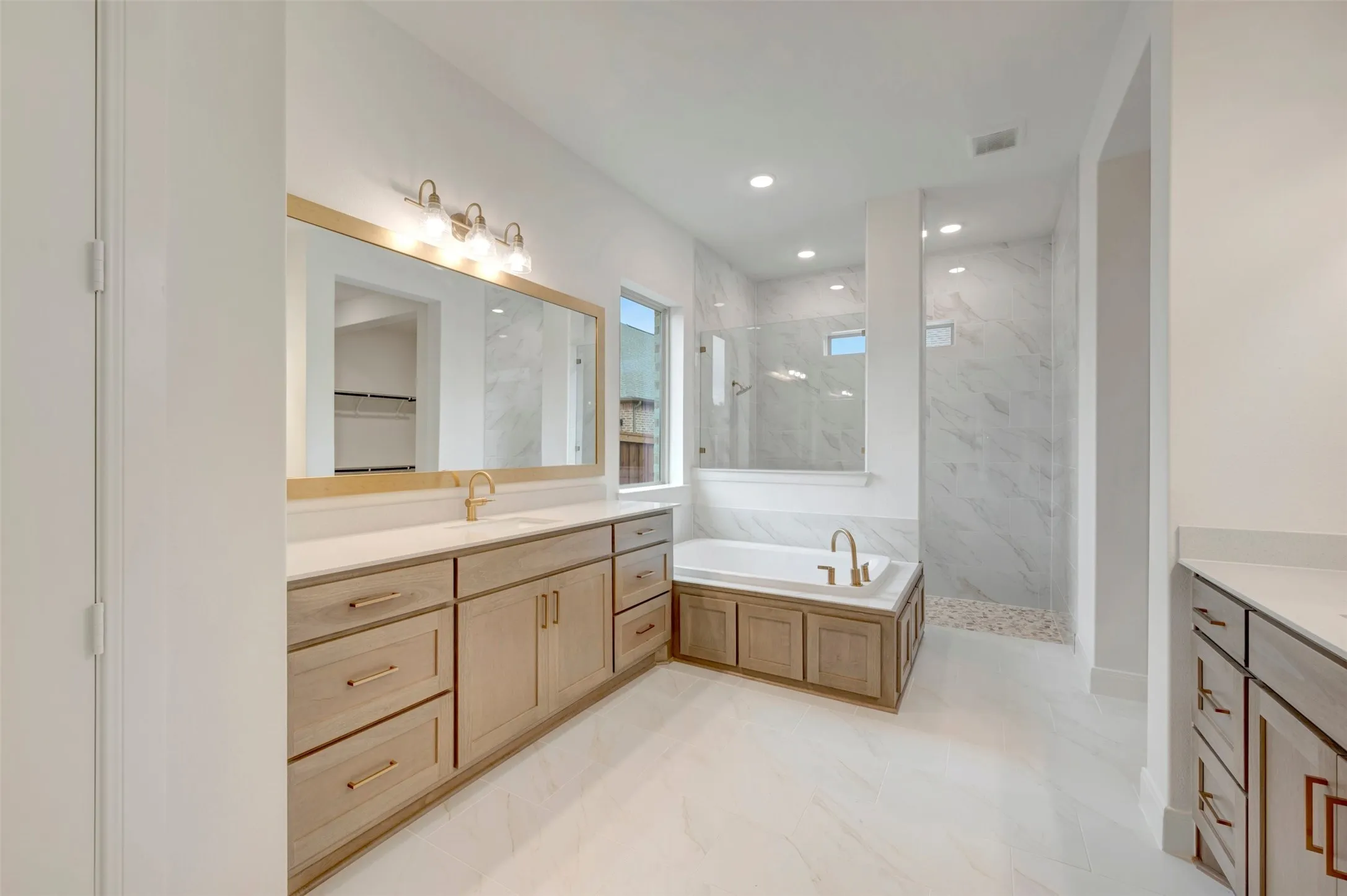 Dual vanity with light wood-finish cabinetry, white countertops, and gold-tone fixtures