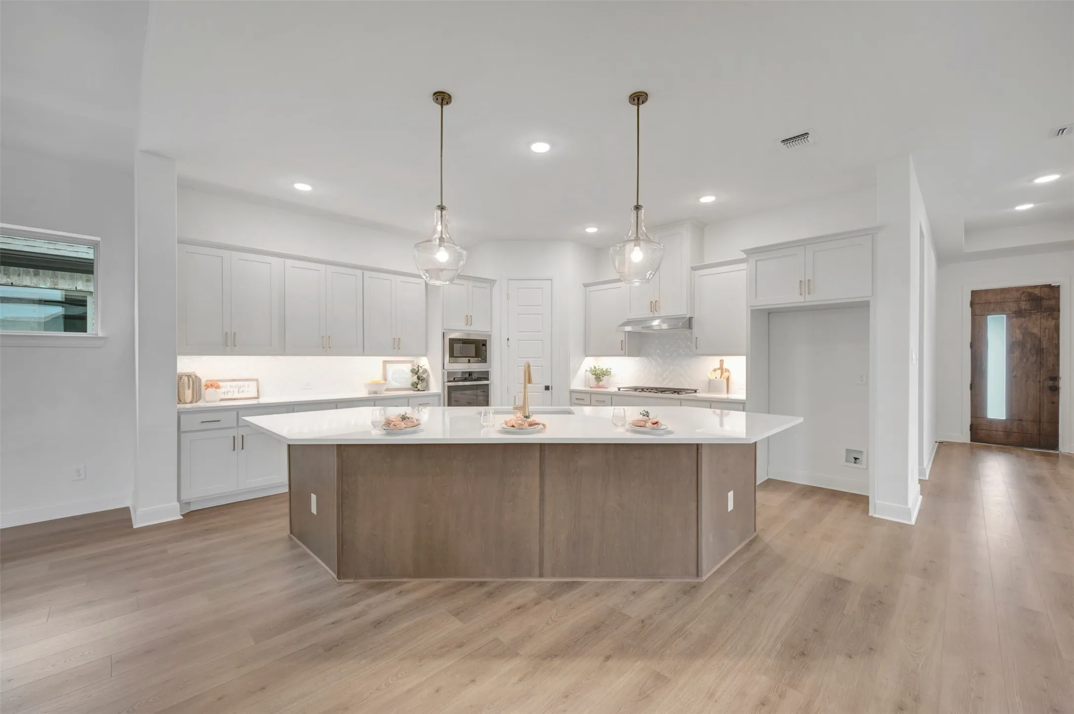 Open-concept kitchen featuring an expansive center island, pendant lighting, built-in stainless steel appliances, white cabinetry, and wood-finish flooring