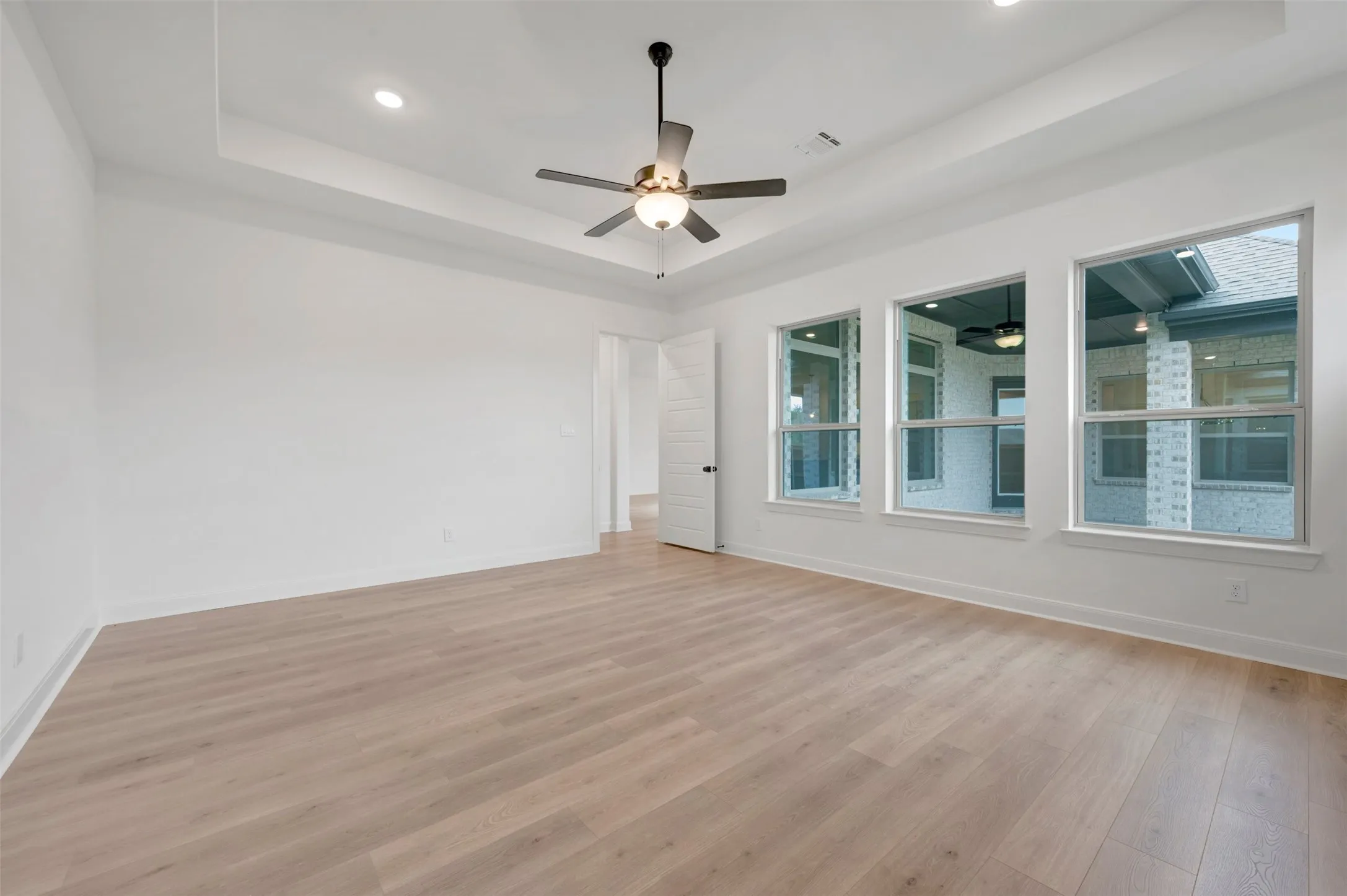 Tray ceiling with recessed lighting and ceiling fan, wood-finish flooring, and multiple windows