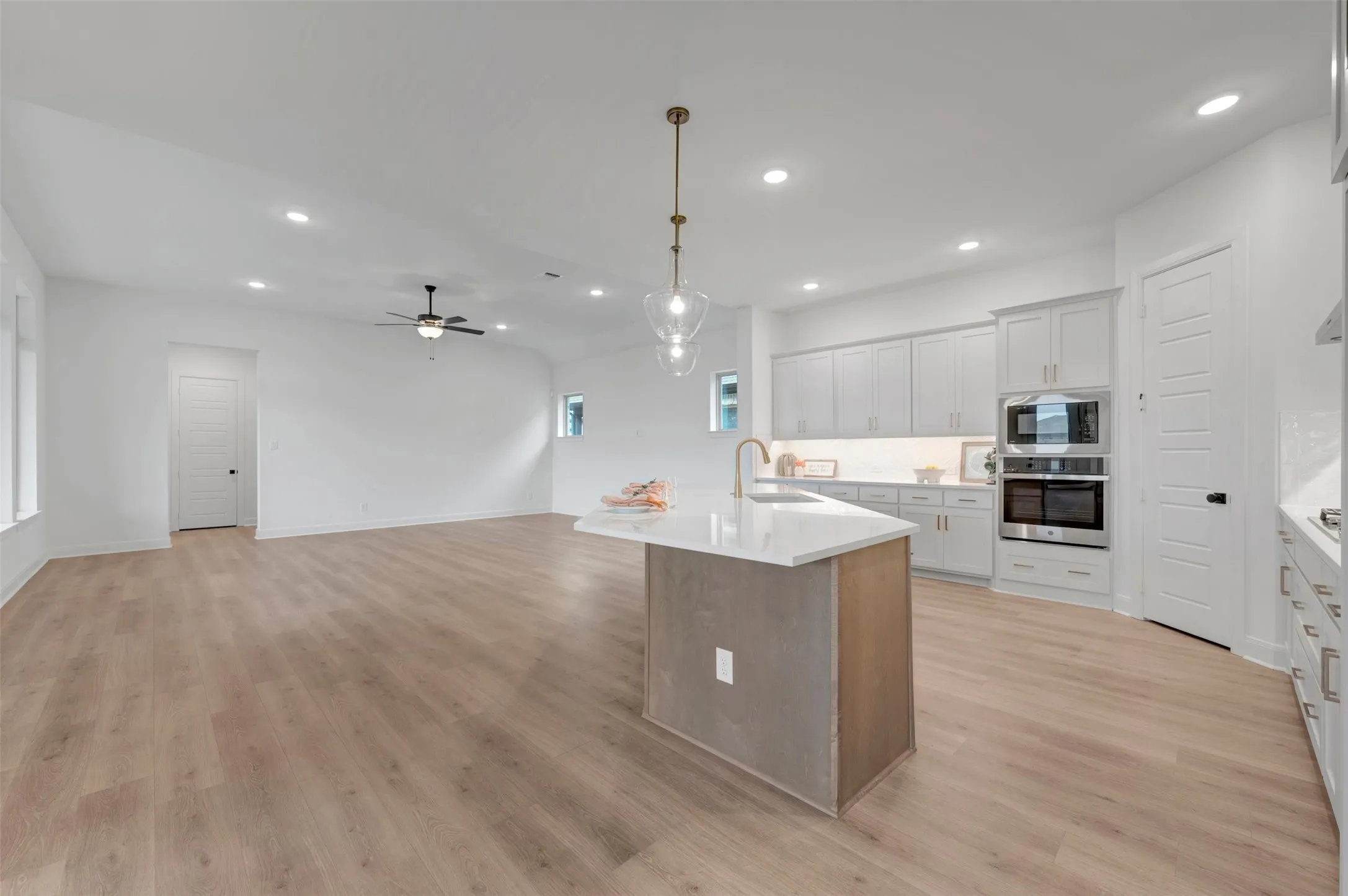 Open-concept living area featuring wood-finish flooring, a kitchen island with a white countertop, recessed lighting, and a ceiling fan
