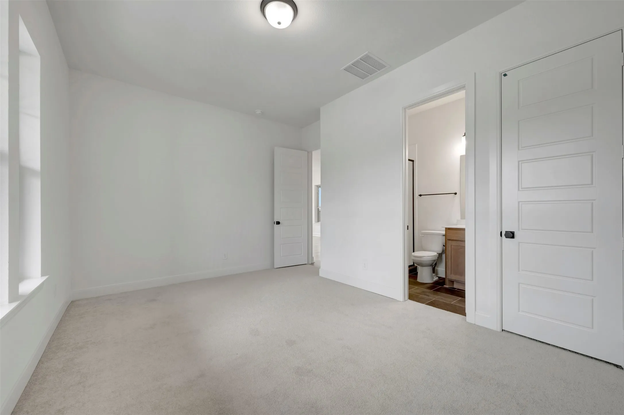 Carpeted flooring, recessed window, paneled interior doors, ceiling-mounted light fixture, and an attached bathroom featuring a vanity with a sink