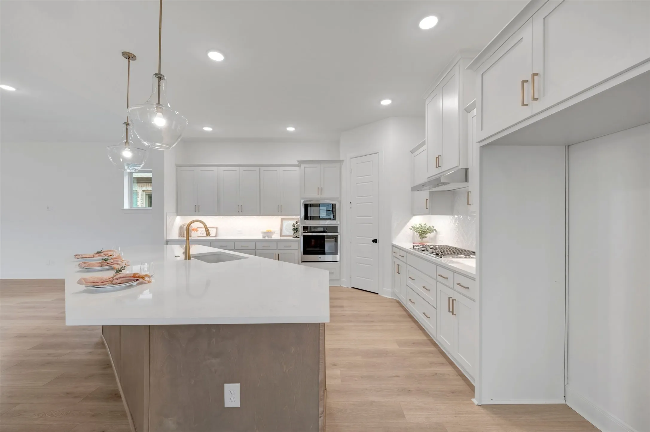 Spacious kitchen featuring an expansive island with a white countertop, two pendant lights, wood-finish flooring, a stainless steel gas range, and a built-in oven