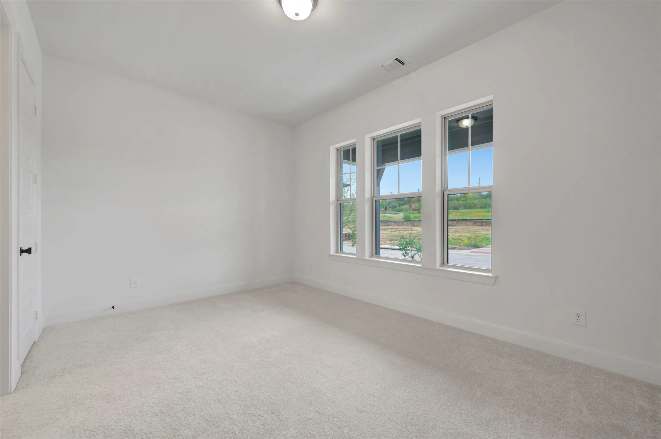 Neutral wall paint, light-toned carpeting, three vertical windows, and a flush mount ceiling light fixture