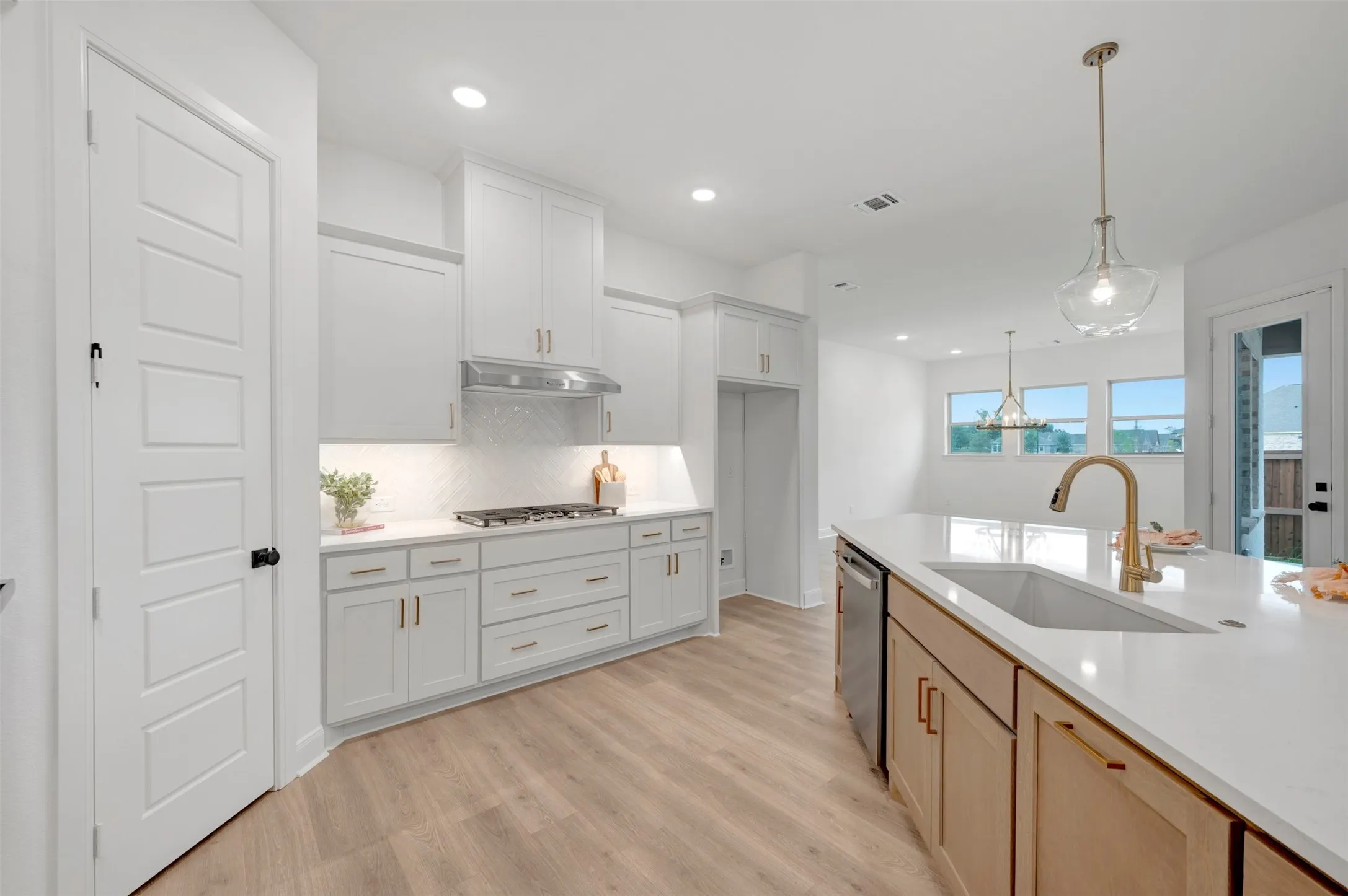 Modern kitchen featuring light wood-finish flooring, white cabinetry with gold-tone hardware, a white countertop island with an undermount sink, and stainless steel appliances