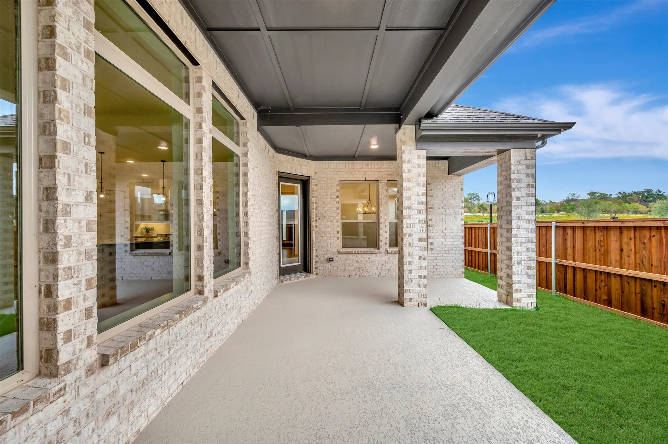 Covered patio featuring a painted concrete surface, brick columns, and a dark-stained wood fence