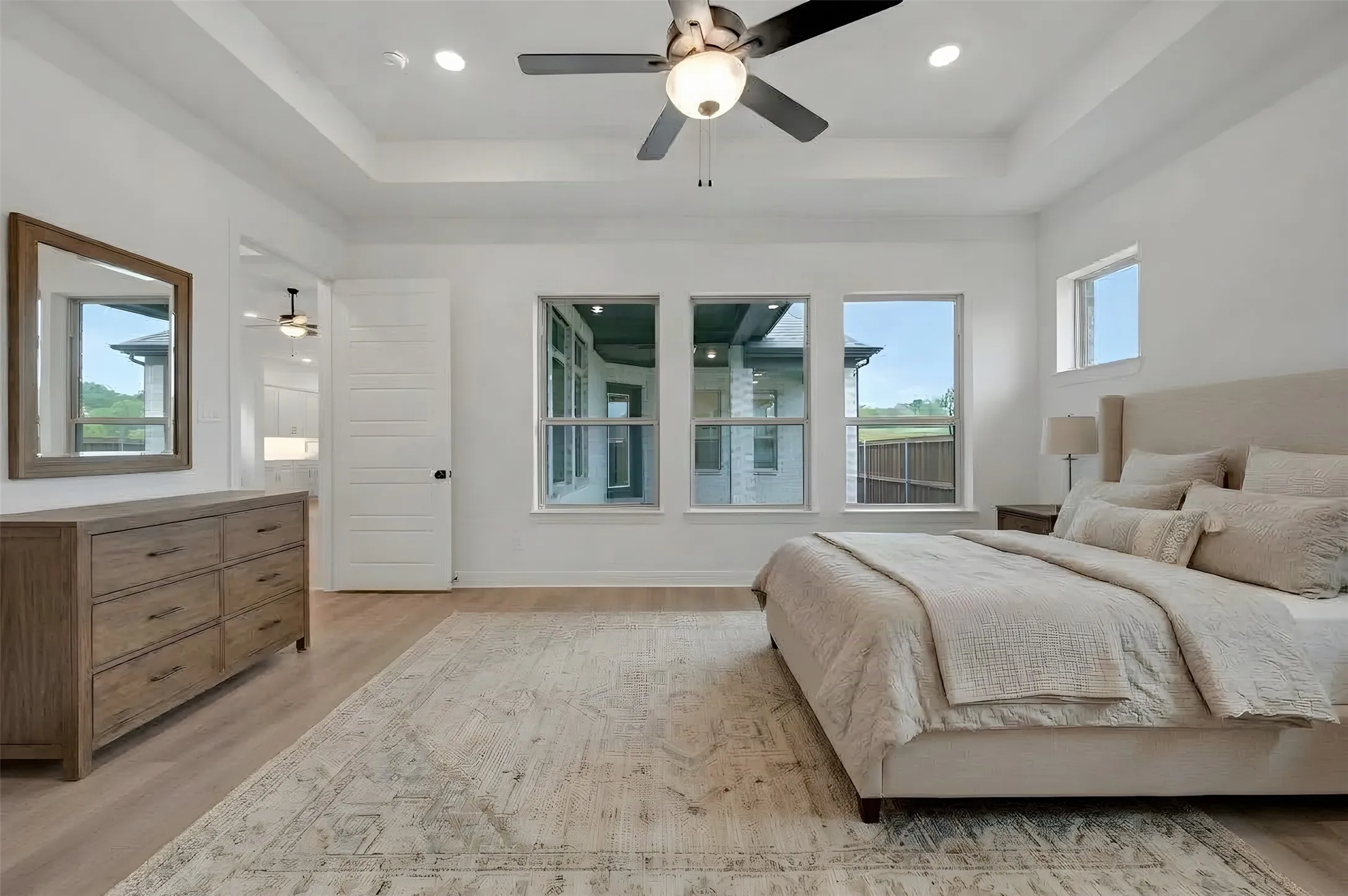 Tray ceiling with recessed lighting and ceiling fan, wood-finish flooring, and multiple windows providing natural light