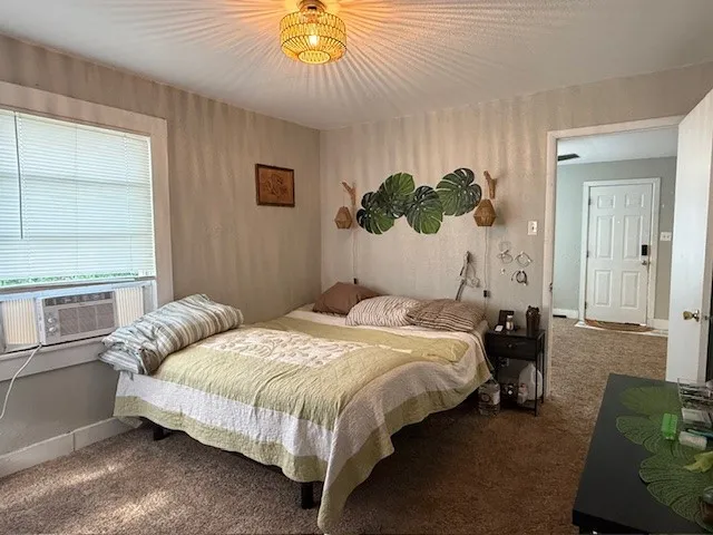Carpeted room with a window-mounted air conditioning unit and a woven pendant light fixture