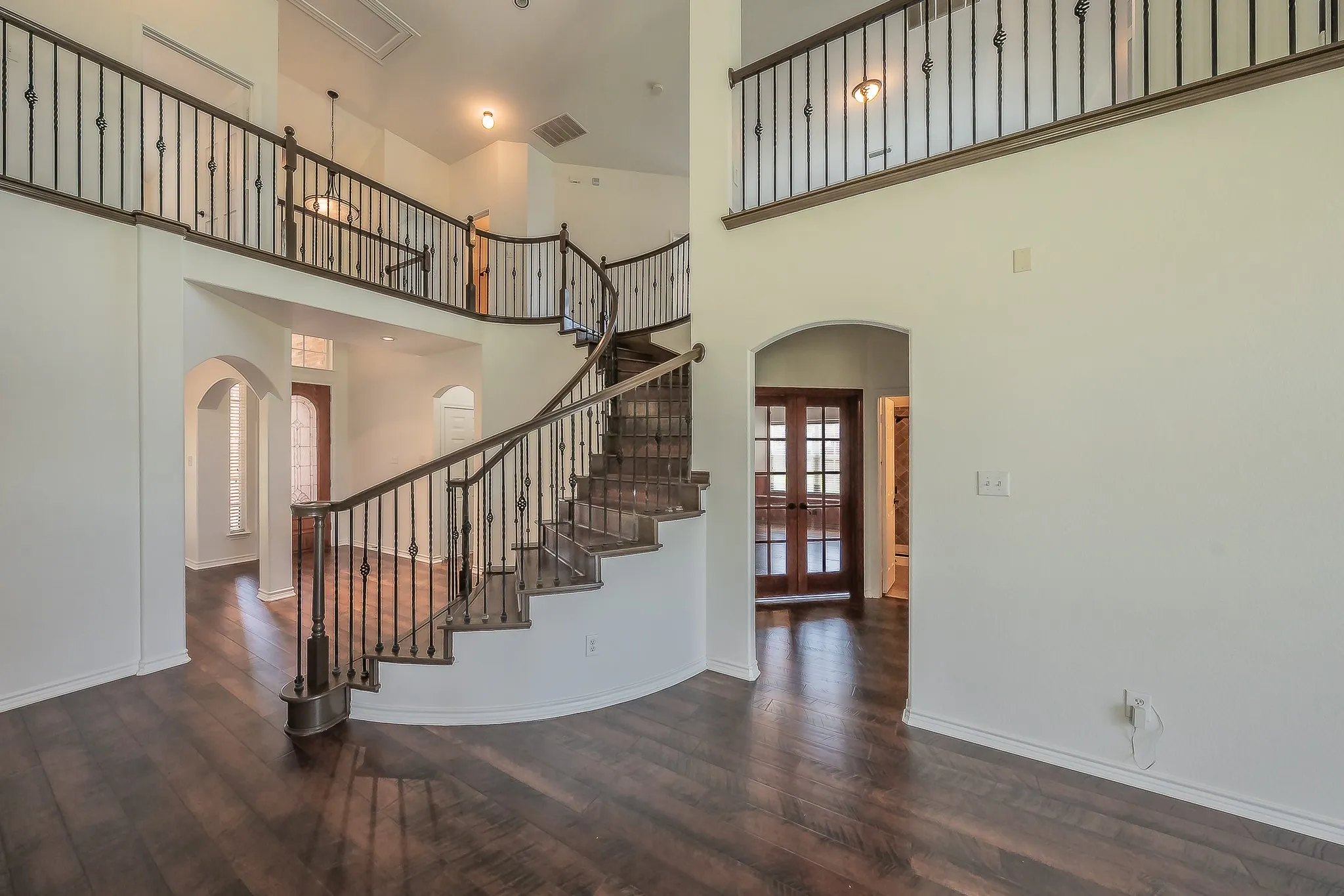 Architectural showcase of the curved staircase with rich wood treads, decorative wrought iron balusters, and open upper balcony with iron railing — a dramatic focal point visible from the foyer and family room.