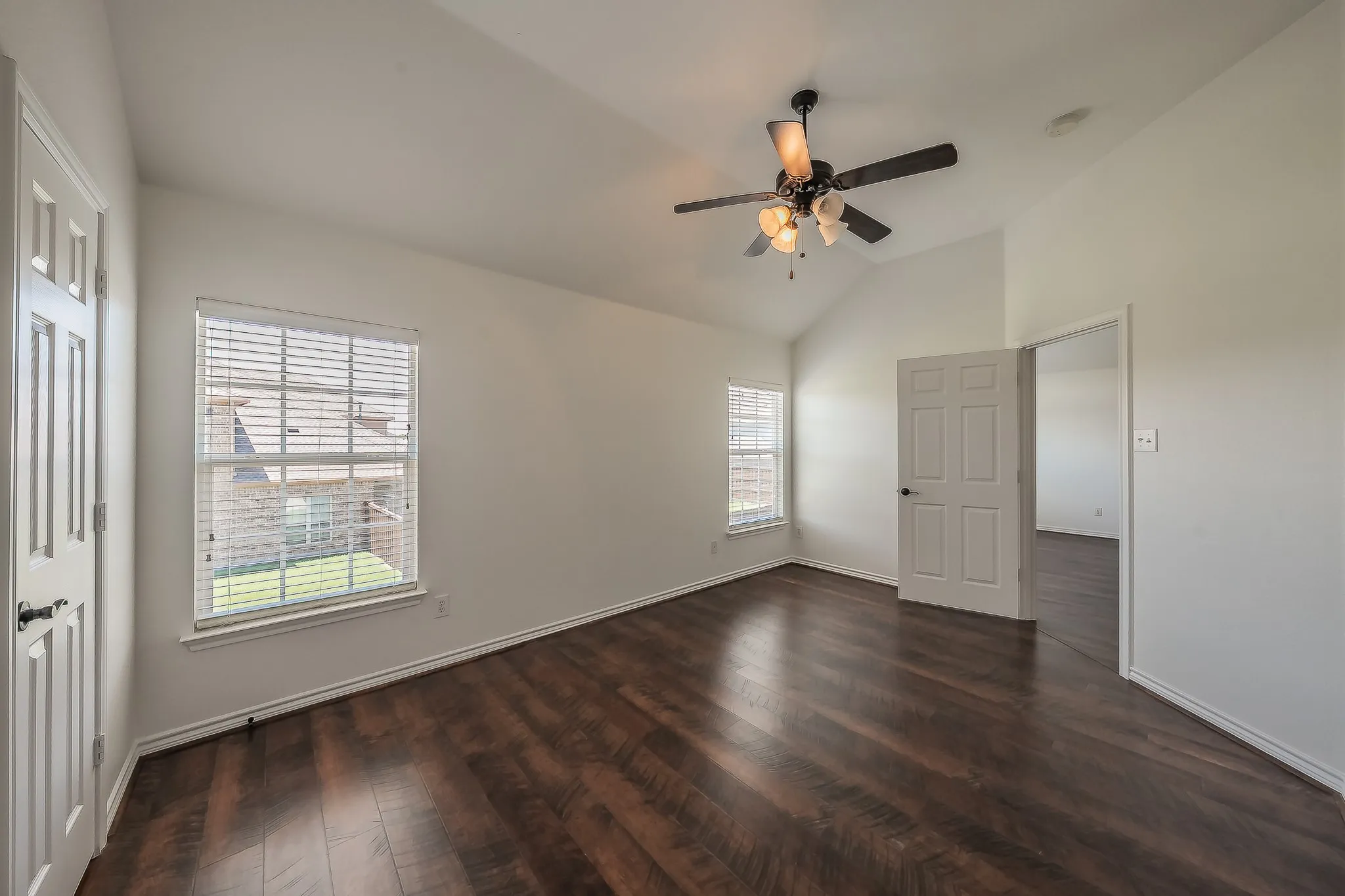 Well-proportioned secondary bedroom featuring a vaulted ceiling, ceiling fan, hardwood floors, two windows, and a pass-through doorway to the adjacent bedroom or hallway.