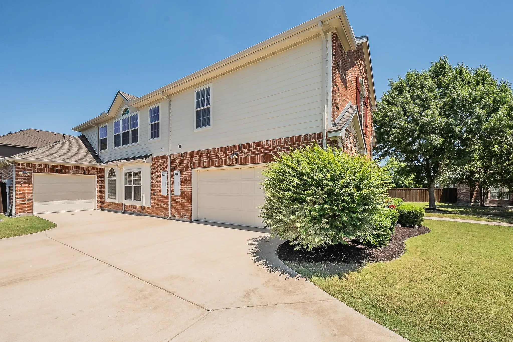 Side elevation featuring a wide concrete driveway leading to the three-car garage with coordinating white doors, brick and siding exterior, and well-maintained foundation plantings.