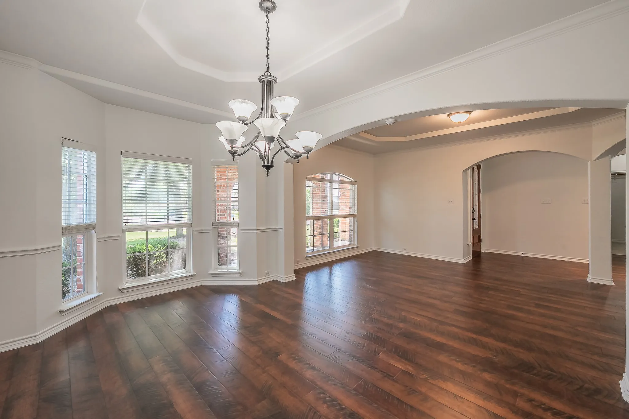 Formal dining room with a curved bay window arrangement flooding the space with natural light, decorative chandelier, tray ceiling, crown molding, and hardwood floors — an impressive setting for entertaining.