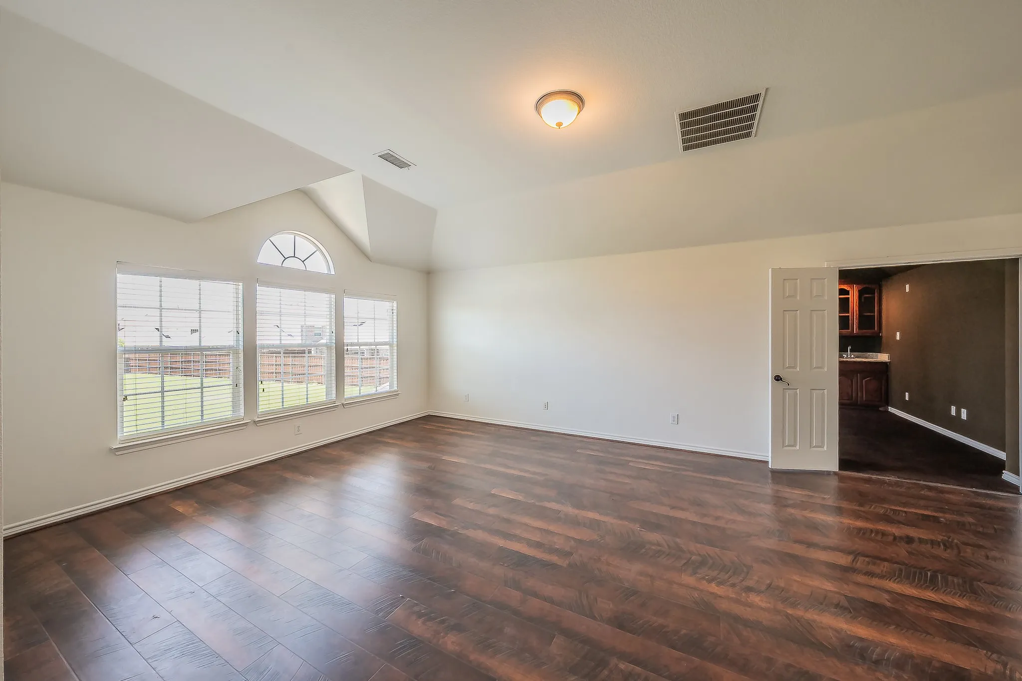 Bright secondary bedroom or flex room on the second floor with vaulted ceiling, arched-top windows, hardwood floors, and a pass-through view into the media/game room wet bar area.