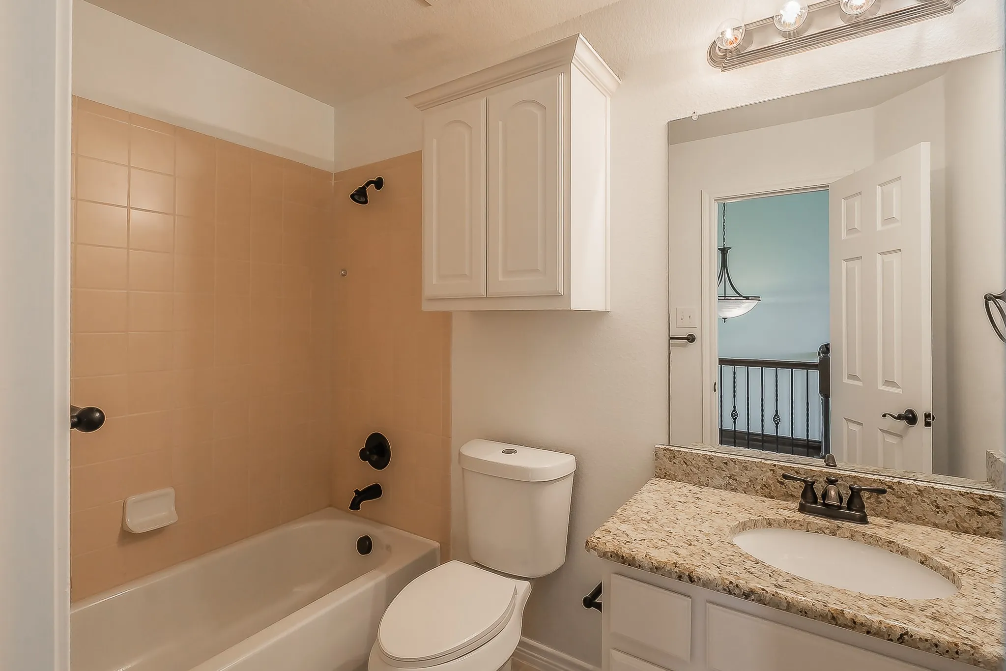 Full secondary bathroom with granite-topped white vanity, large mirror, oil-rubbed bronze fixtures, tile tub-shower combo, tile flooring, and upper cabinet storage — clean and well-maintained.