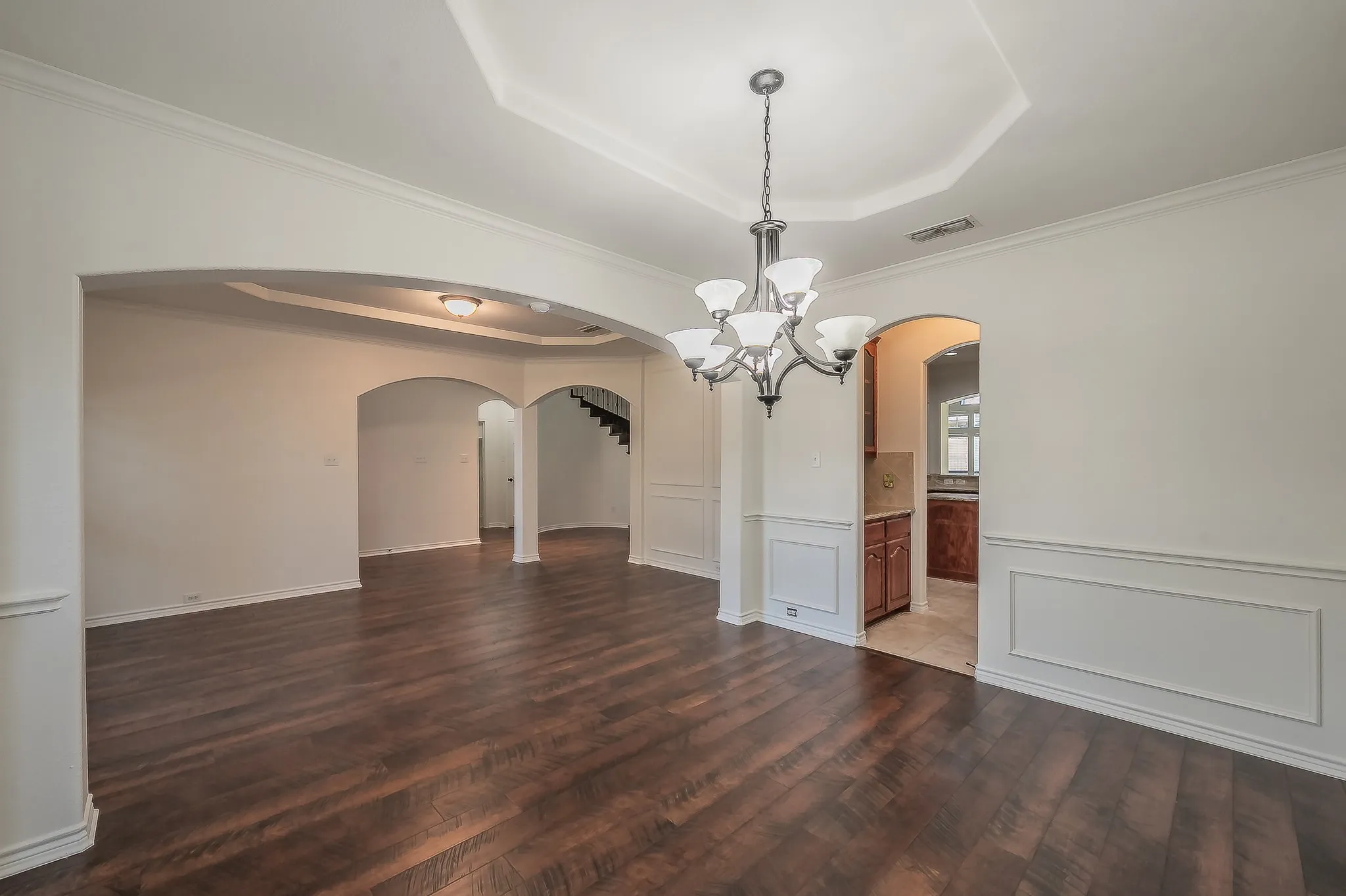 From the dining room looking through multiple arched openings toward the formal living room and kitchen with a glimpse of cherry cabinetry and the casual dining nook beyond.